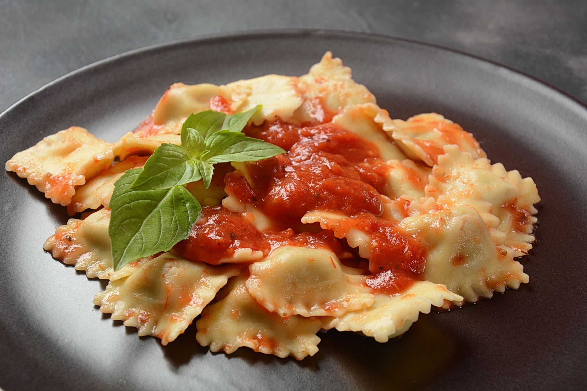 Une assiette de raviolis Tortoliesi servie sur une assiette noire avec une feuille de basilic
