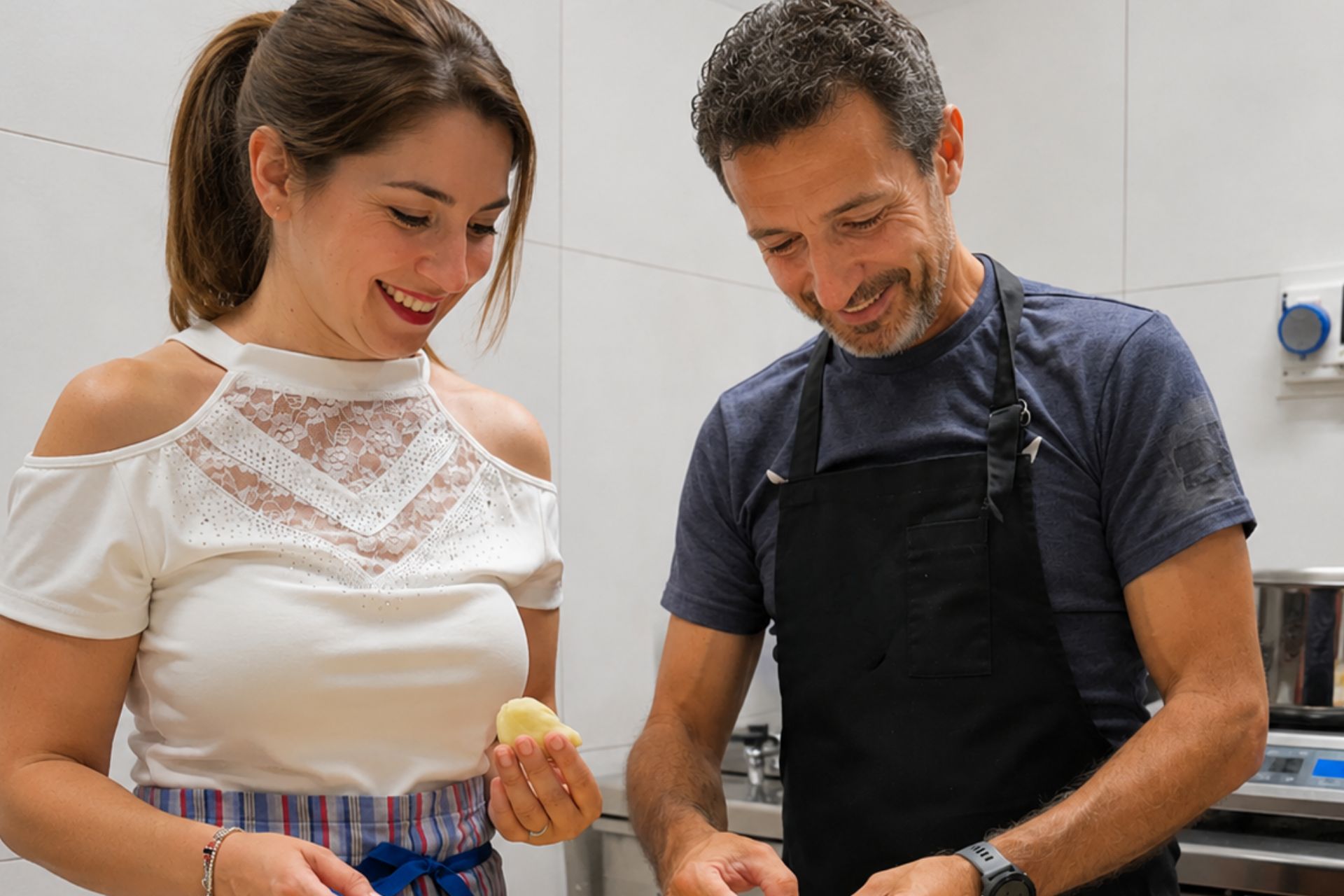 Eine Frau und ein Mann in der Küche bereiten lächelnd Seadas, ein typisch sardisches Dessert, in einer einladenden Umgebung zu