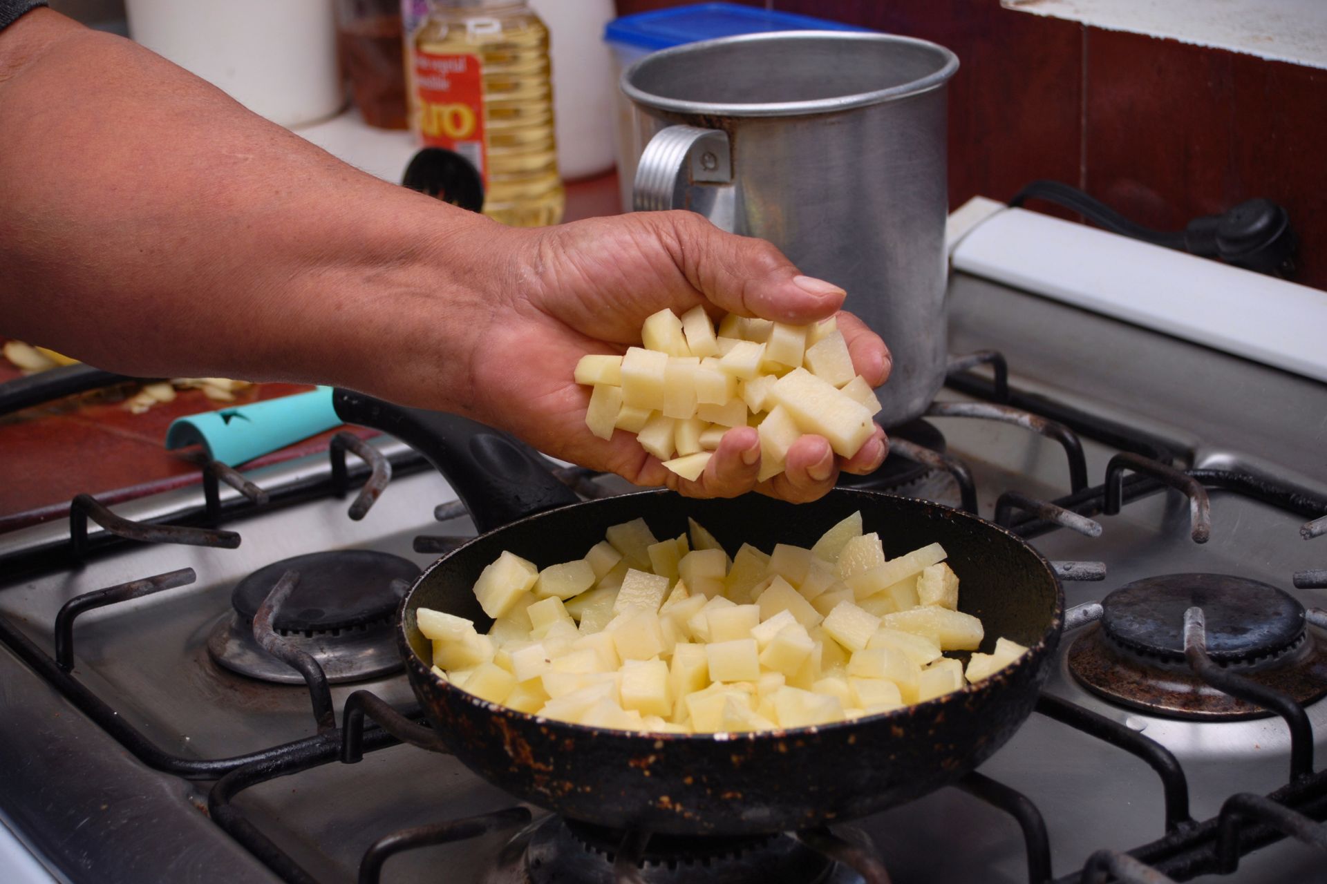 Eine Person gibt Kartoffelwürfel in eine Pfanne auf einem Gasherd