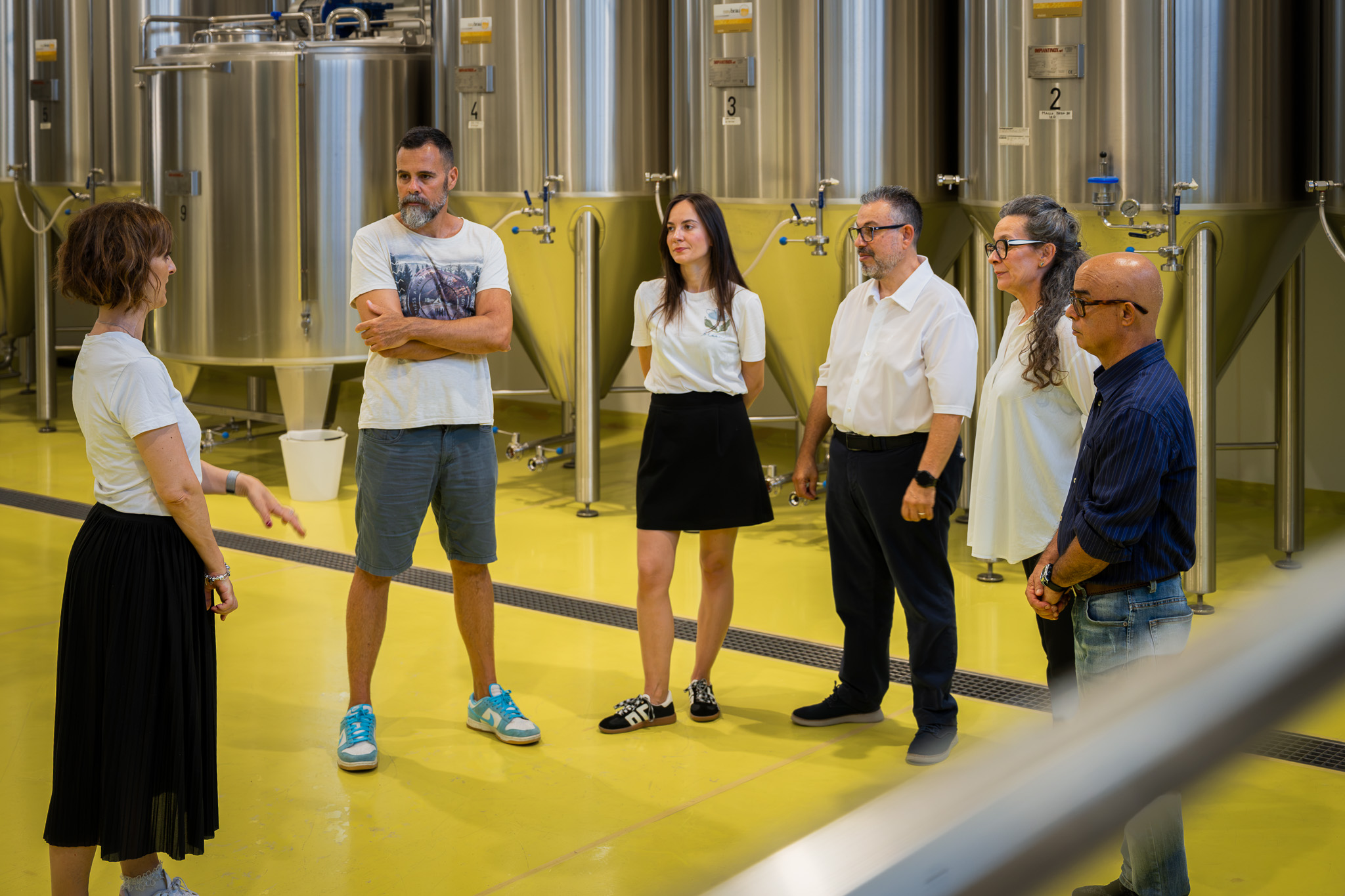 Persone in visita ad un birrificio con fermentatori in acciaio in vista