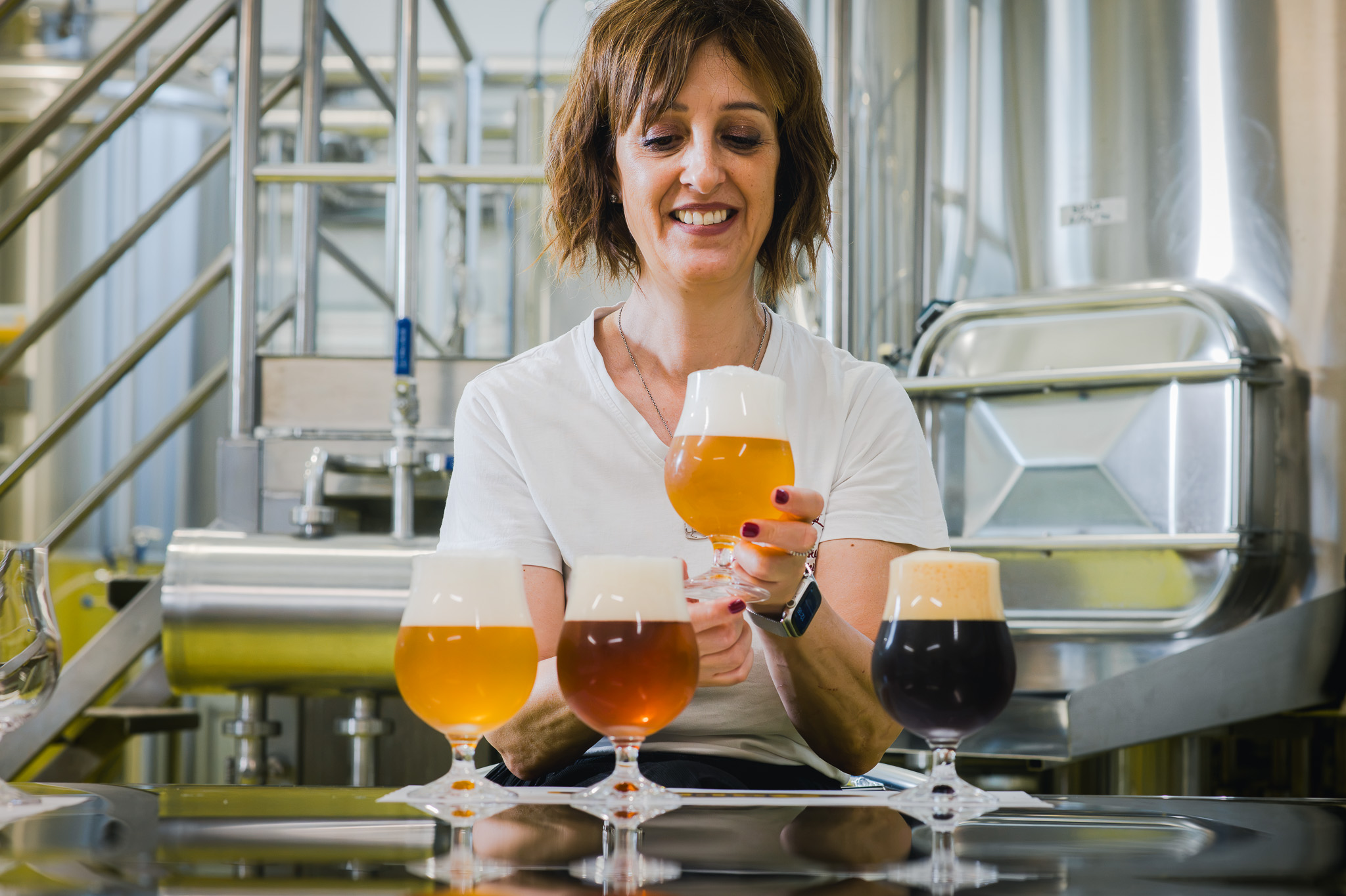 Una donna in un birrificio tiene in mano un bicchiere di birra artigianale, con altri tre bicchieri di birra davanti a lei.
