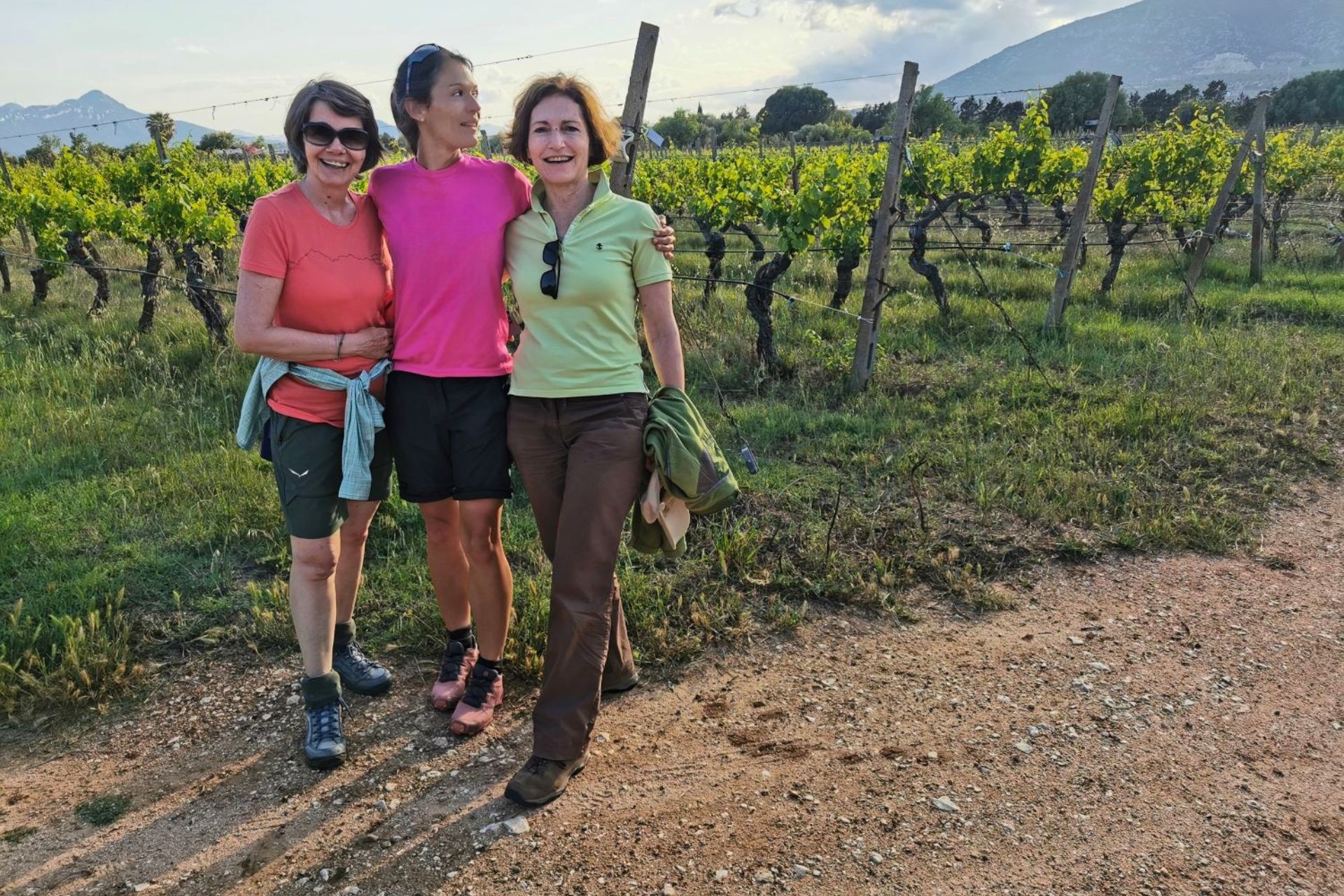 Tres mujeres sonrientes en un paisaje de viñedos y montañas