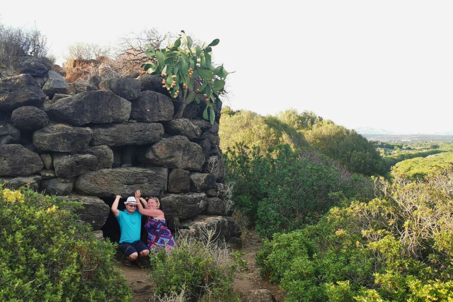 Dos personas se sientan frente a una estructura de piedra con un cactus