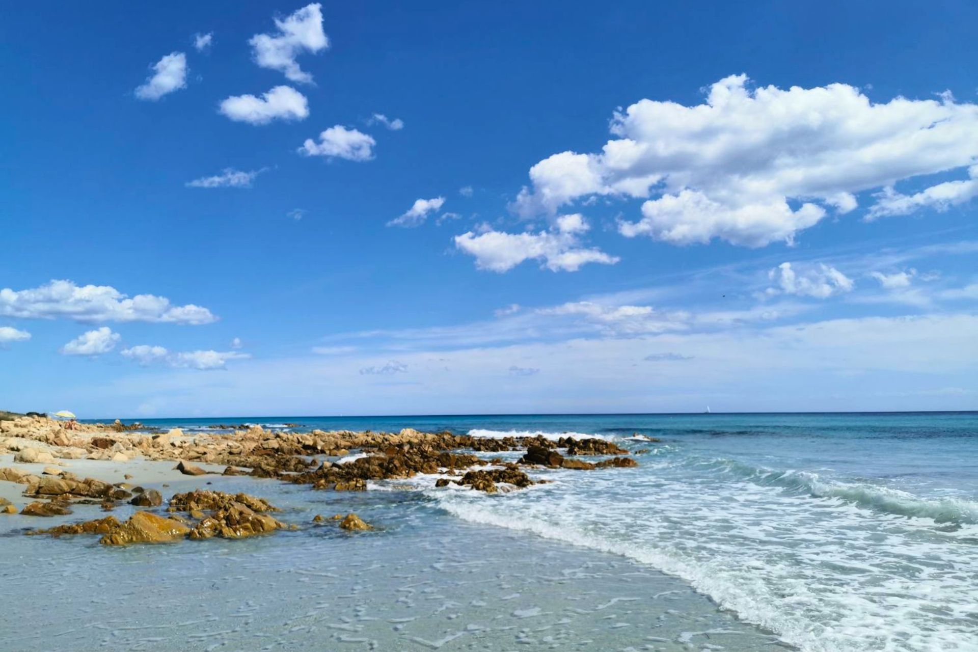 Strand mit Felsen und blauem Meer unter blauem Himmel mit Wolken
