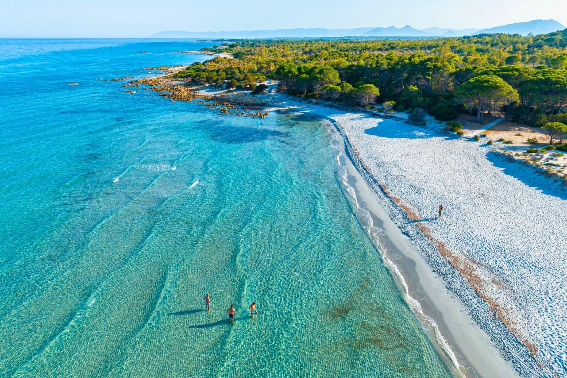 Une plage de sable blanc et d'eau cristalline avec quelques visiteurs dans l'eau et un visiteur sur la plage