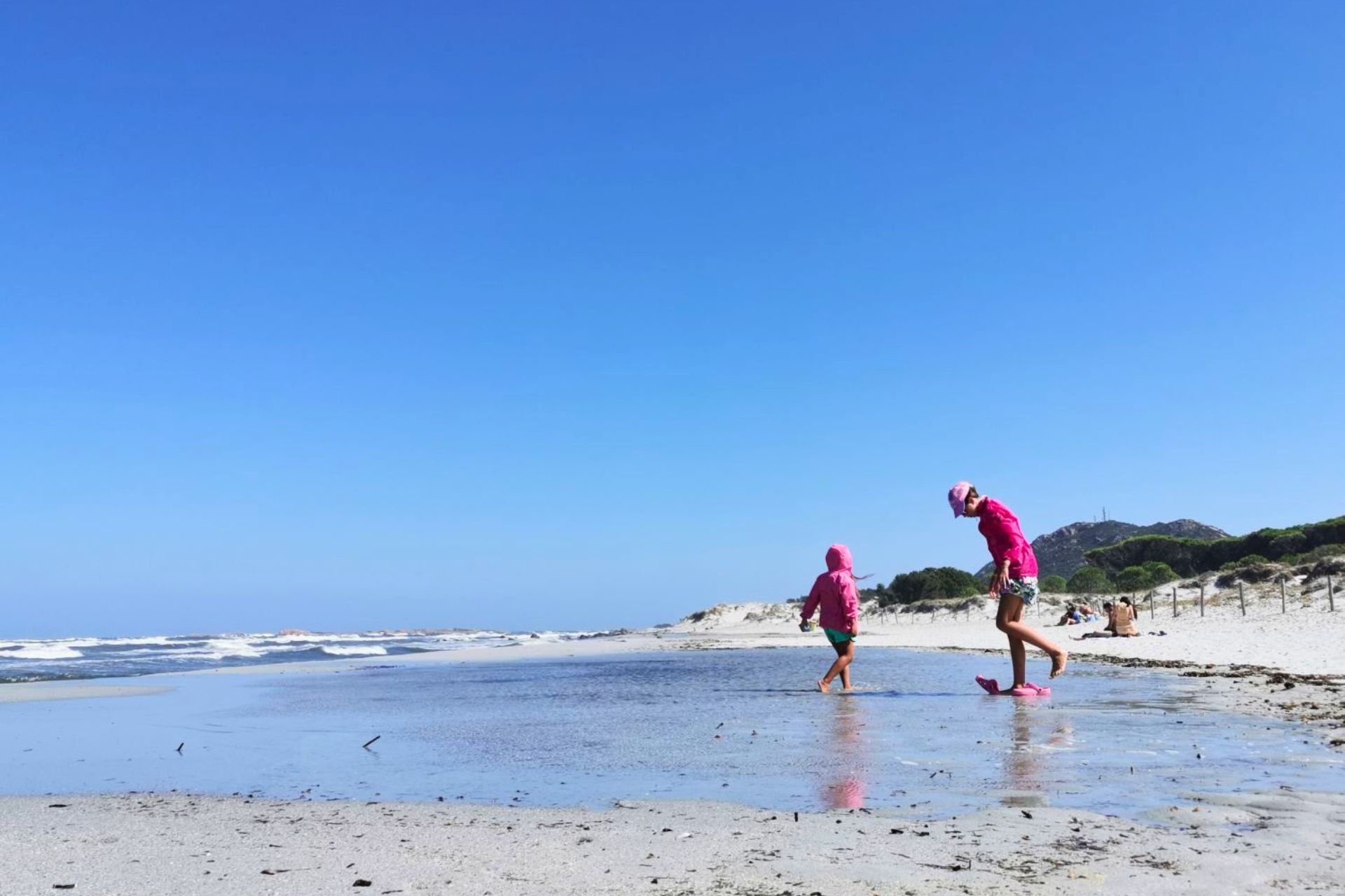 Deux personnes en rose marchant sur la plage d'une côte avec mer calme et ciel bleu