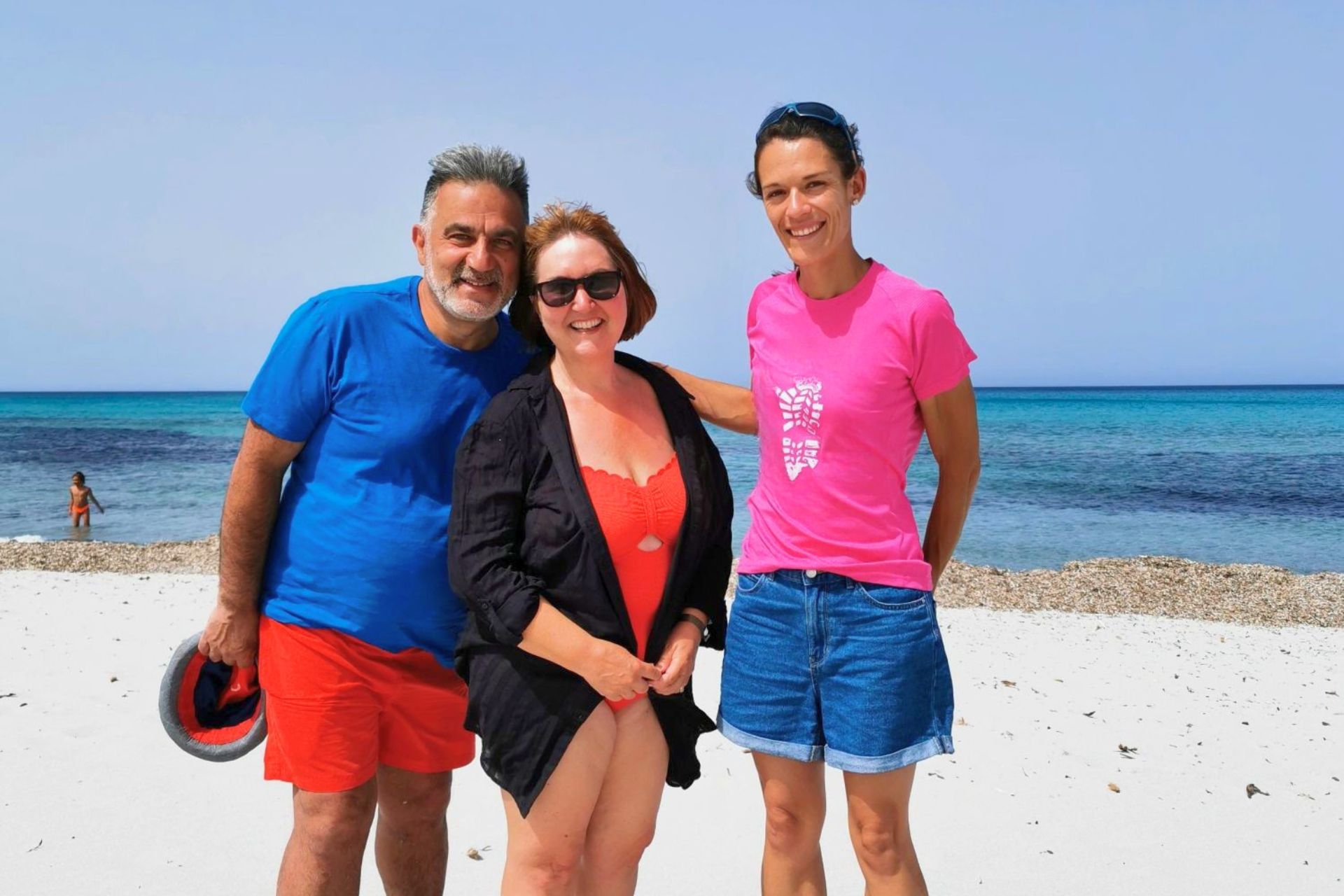 Trois personnes debout sur une plage avec une mer calme en arrière-plan