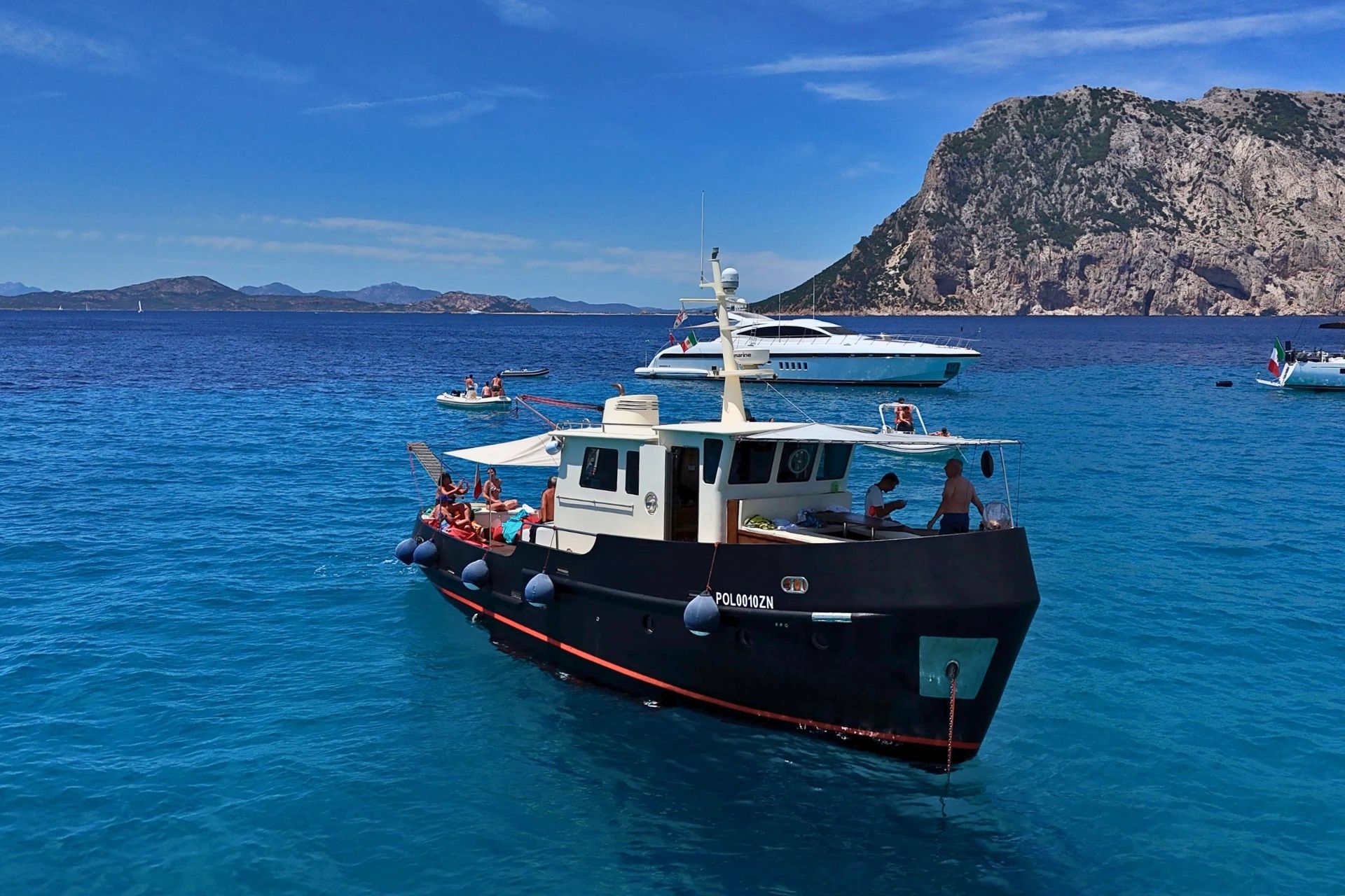 Bateau vintage avec des personnes à bord et d'autres bateaux dans une baie bleue avec des montagnes en arrière-plan