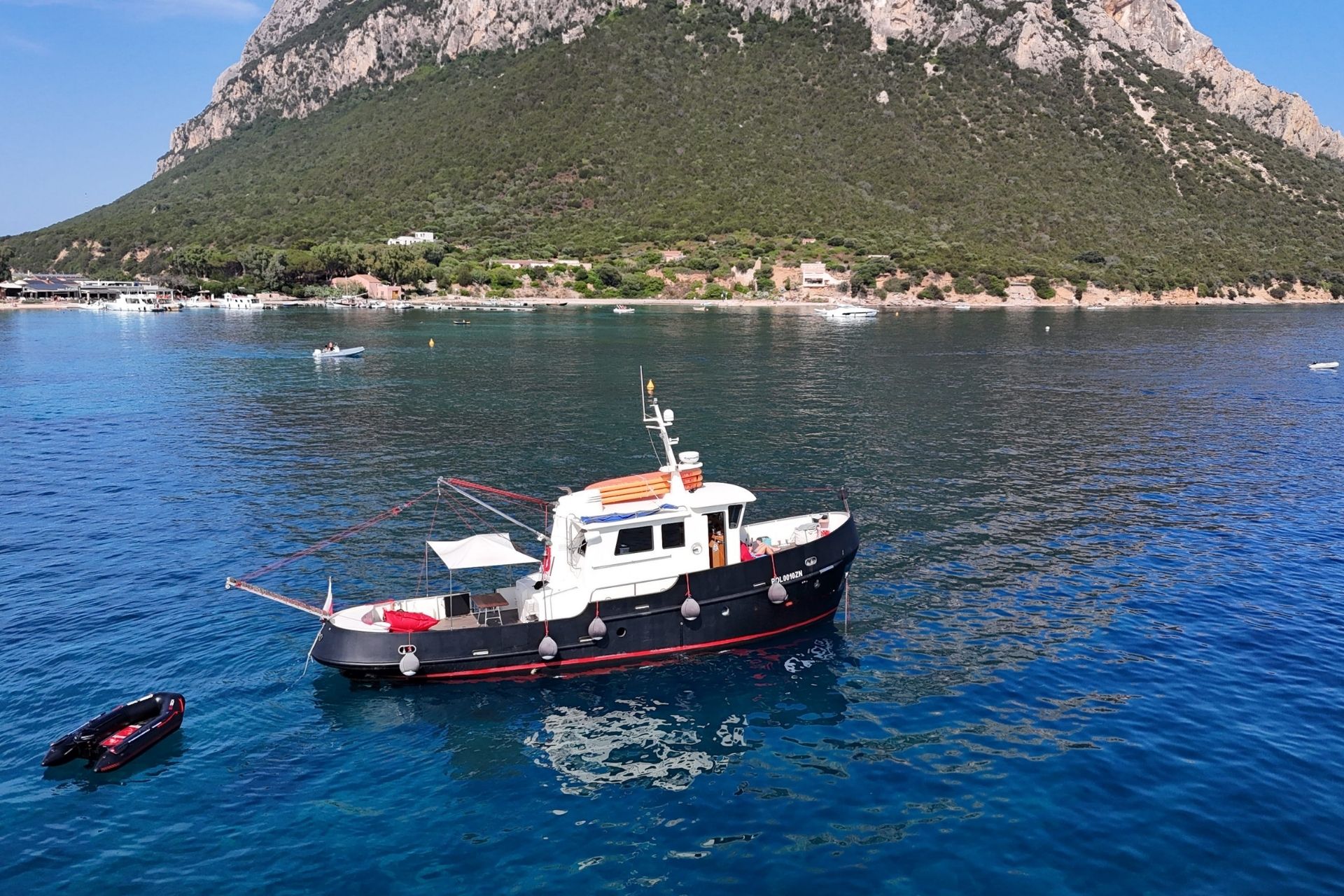 Image d'un bateau à moteur d'époque amarré dans une mer limpide avec une île verdoyante en arrière-plan.