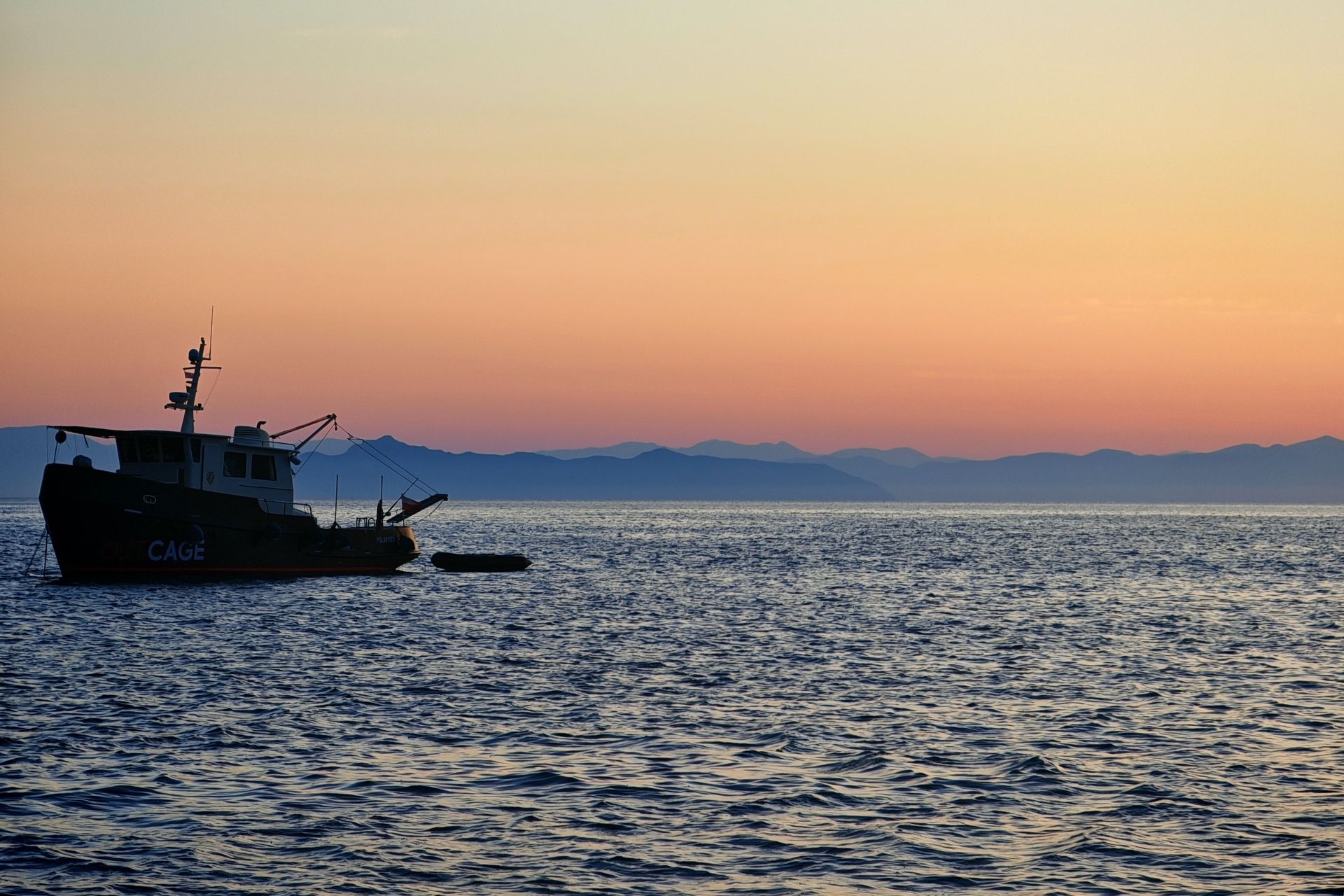 Photo d'un bateau à moteur vintage naviguant sur la mer avec des montagnes en arrière-plan au coucher du soleil