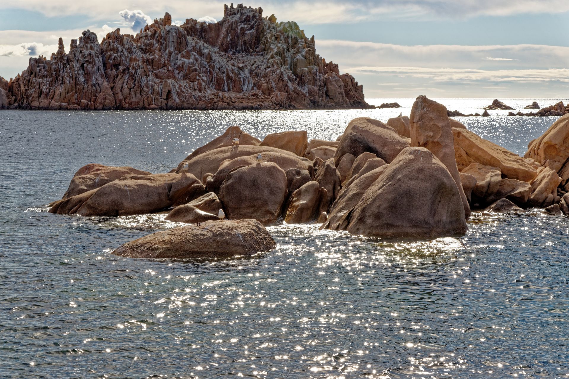 Immagine di una costa rocciosa con scogli e mare calmo con un gommone ormeggiato