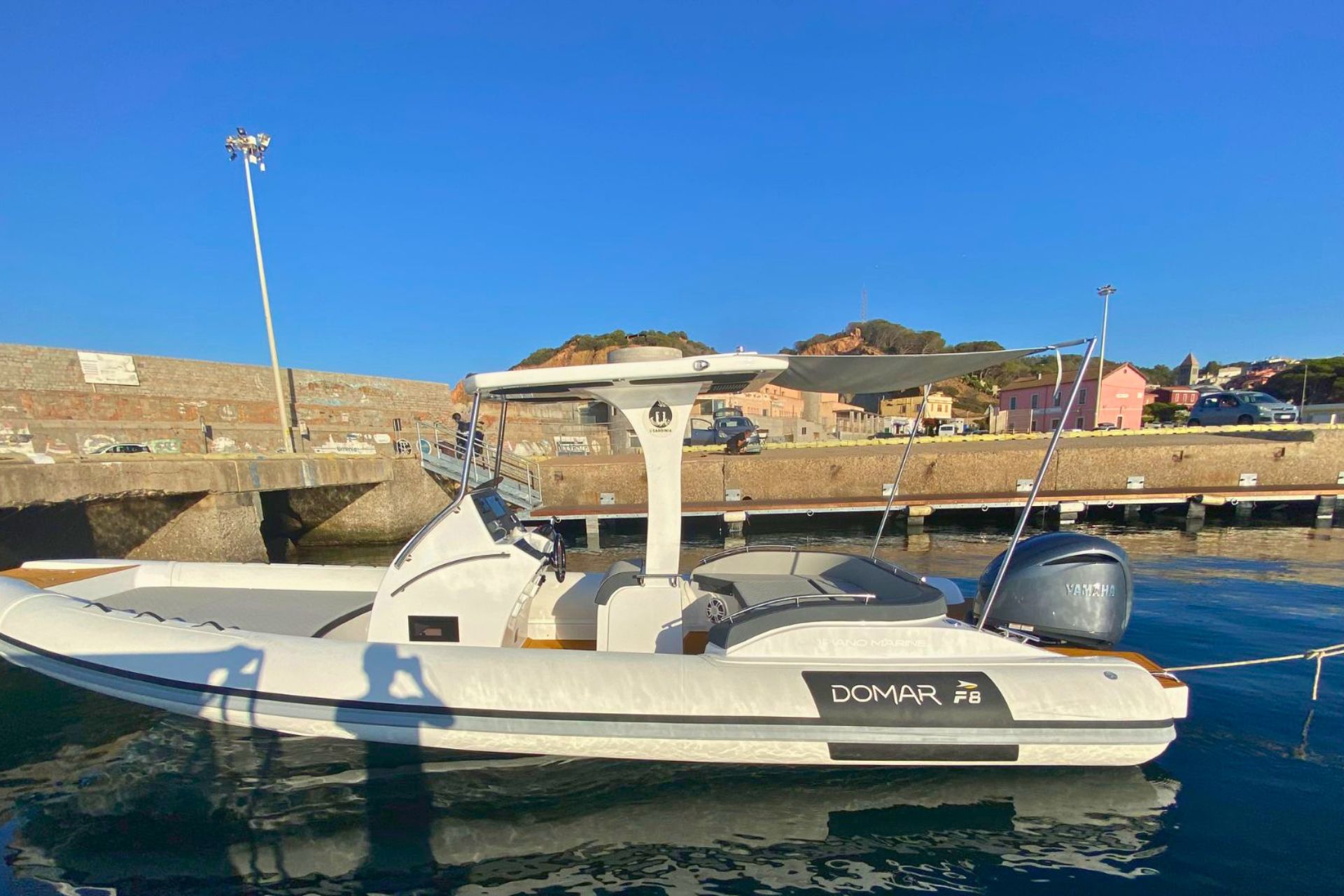Immagine di un gommone bianco ormeggiato al porto con sullo sfondo edifici e una collina