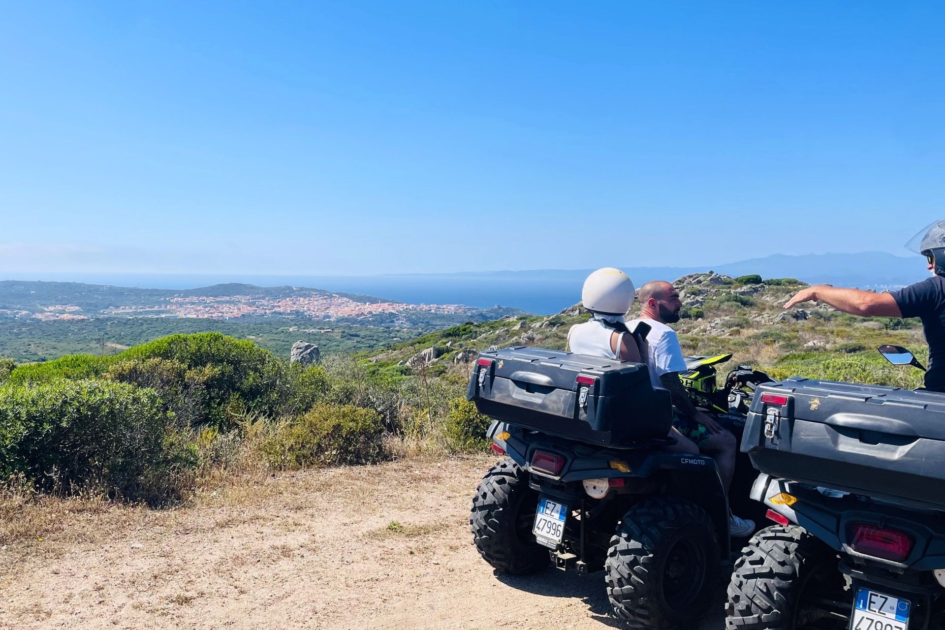 Tre persone in moto fuoristrada su un sentiero panoramico con vista sul mare e sulla costa