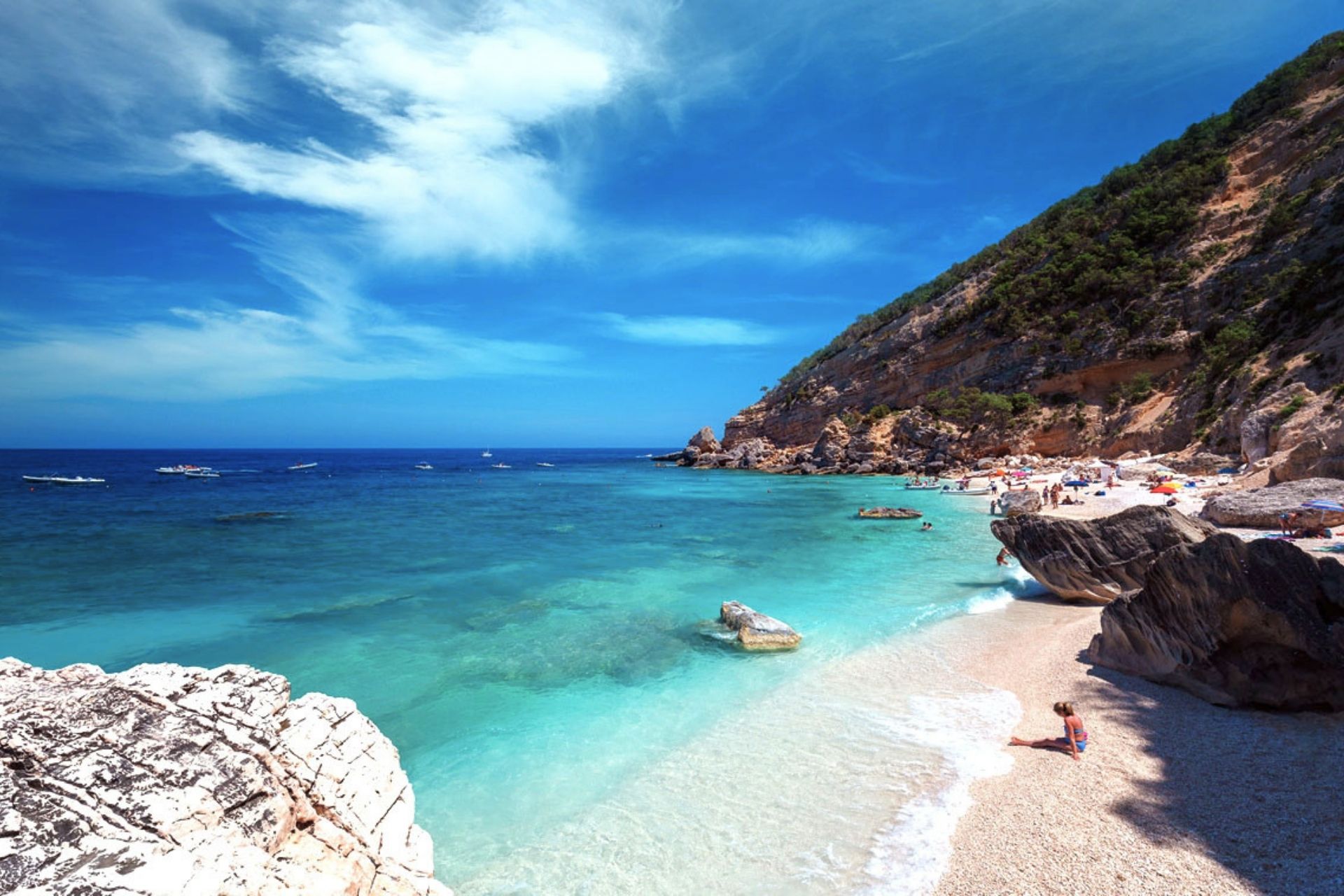 Une plage avec des falaises rocheuses, une mer cristalline et quelques personnes prenant un bain de soleil et nageant.