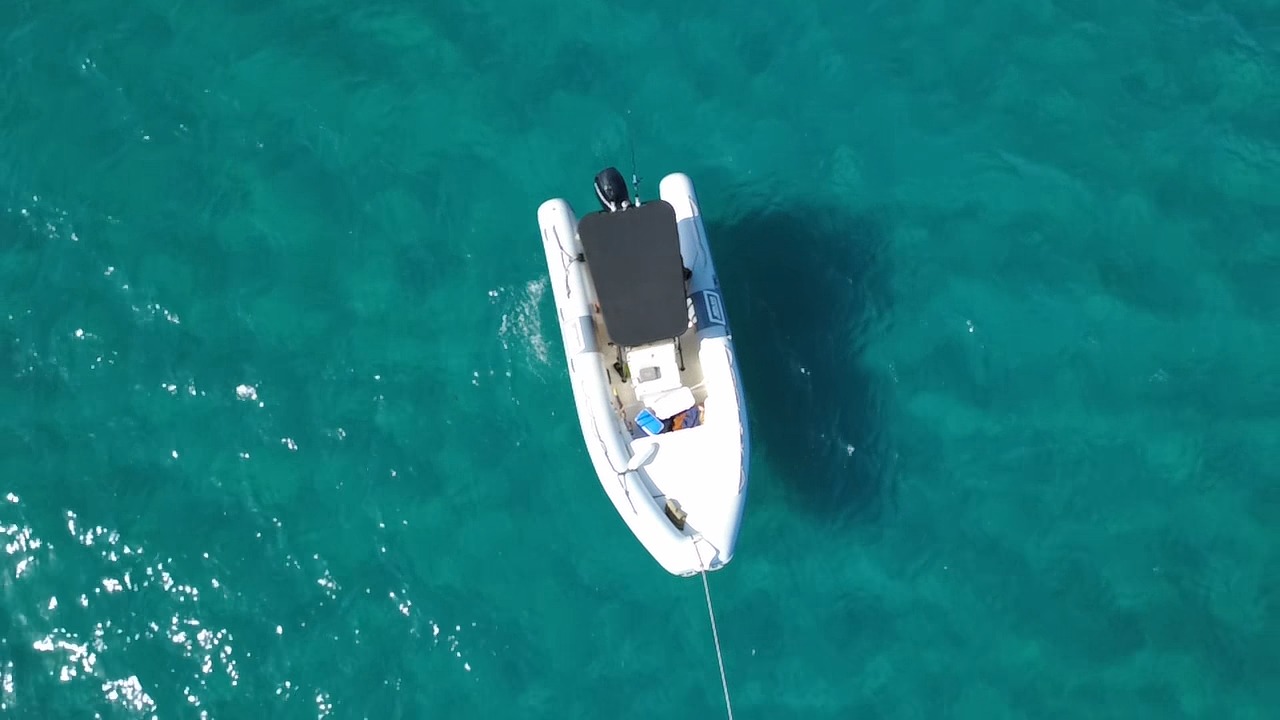 Image of a dinghy with a black cover in blue water with reflections of the sun.