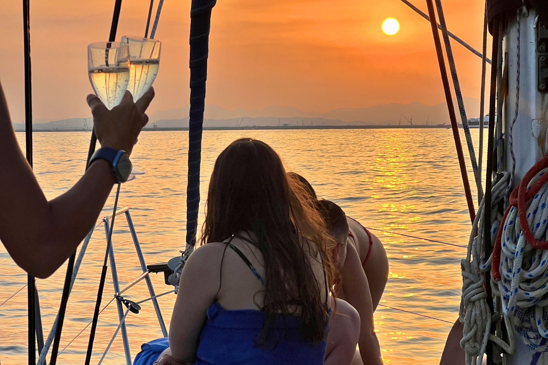 Group of people on a sailboat with coves and sunset in the background
