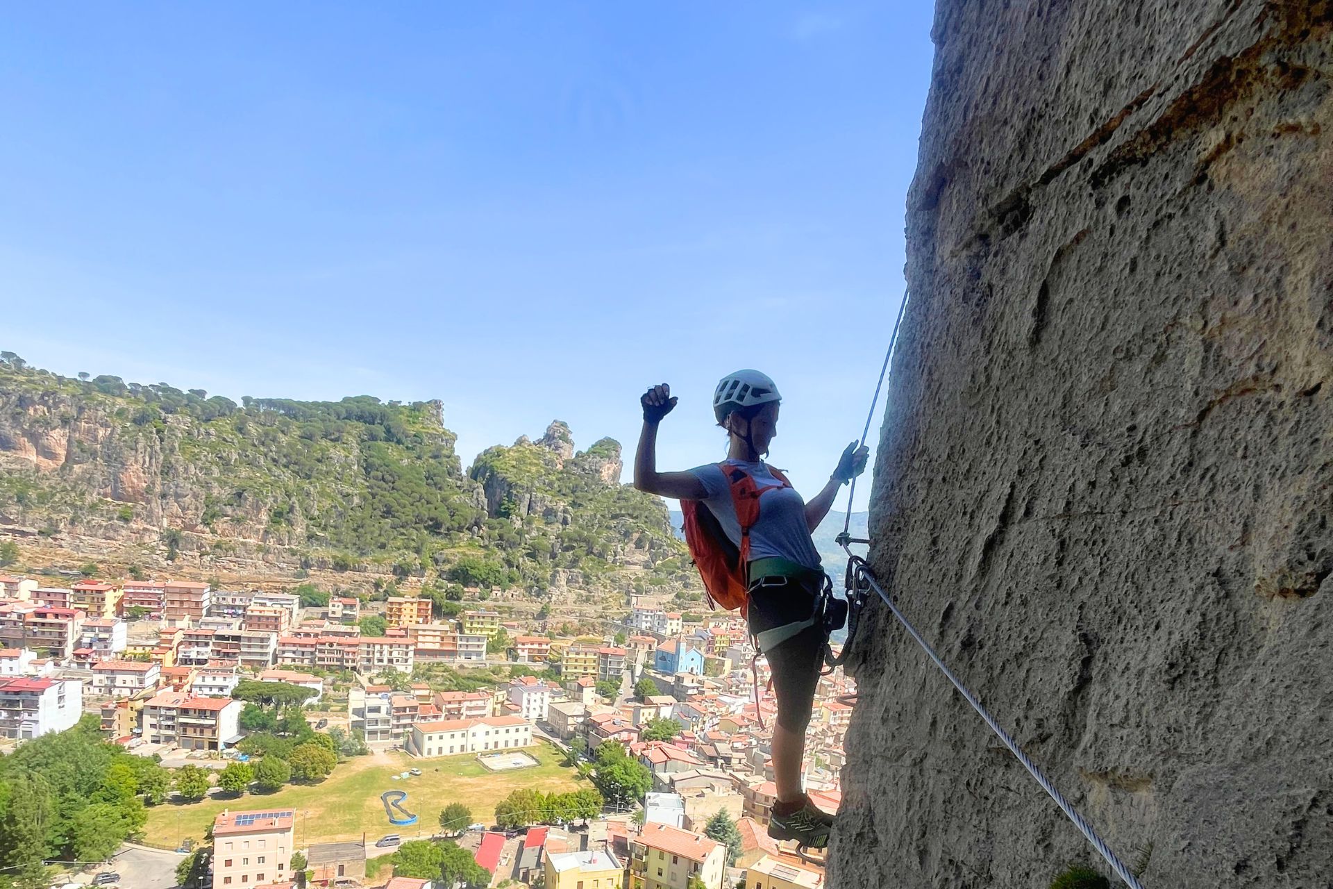 Eine Person klettert auf eine Felswand mit Blick auf ein Dorf darunter und Berge in der Ferne
