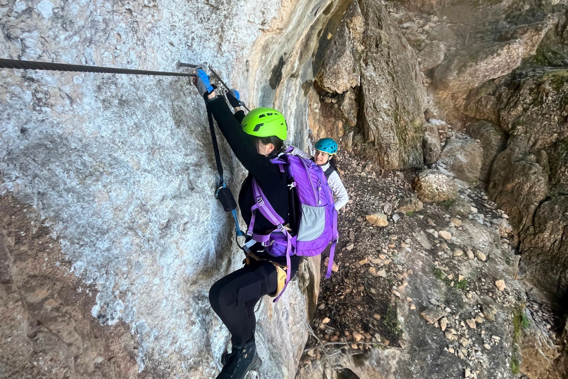 Zwei Personen mit Kletterausrüstung an einer Felswand, mit einem Sicherheitskabel