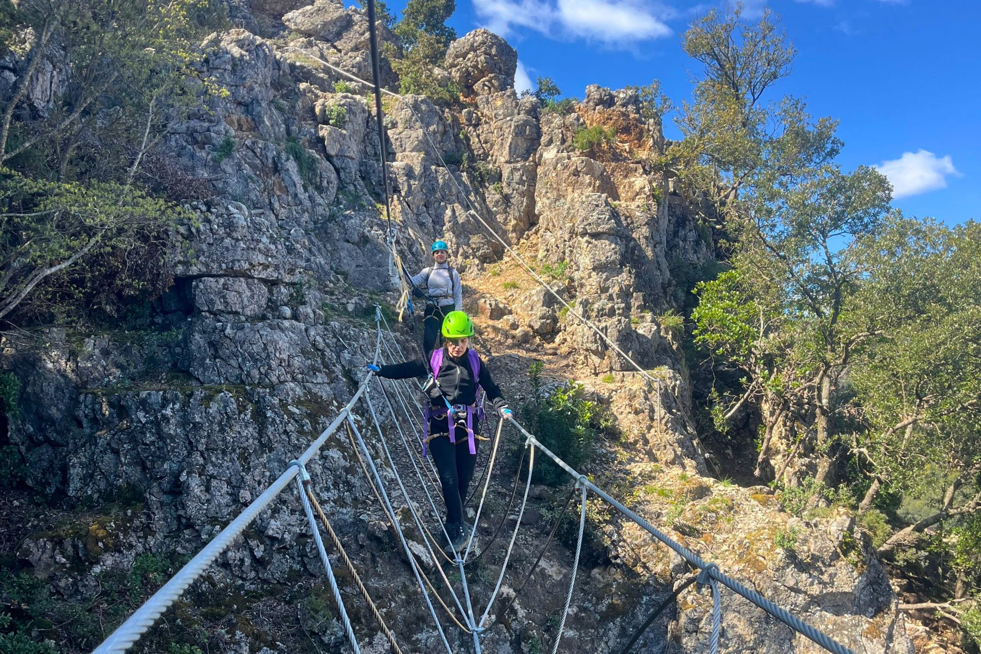 Zwei Personen in Kletteranzügen und Helmen, die auf einem Klettersteig zwischen den Felsen laufen
