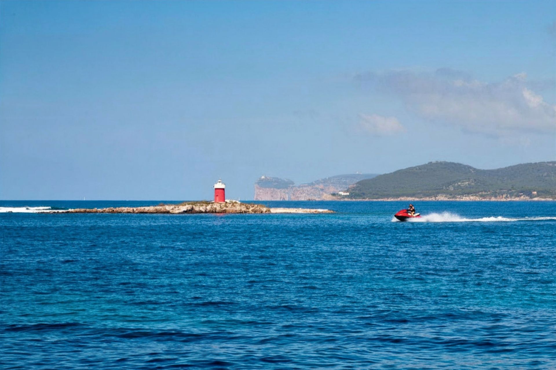 A person riding a jet ski hurtles across the blue sea