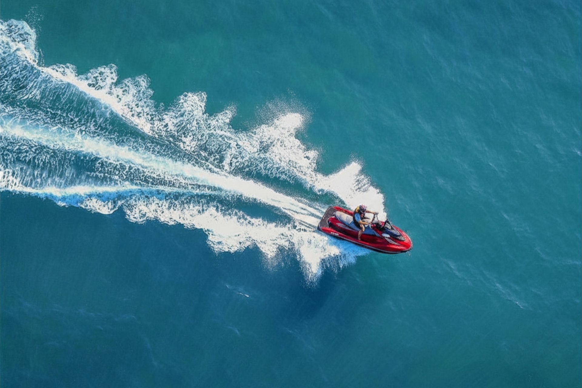 A person riding a jet ski hurtles across the blue sea