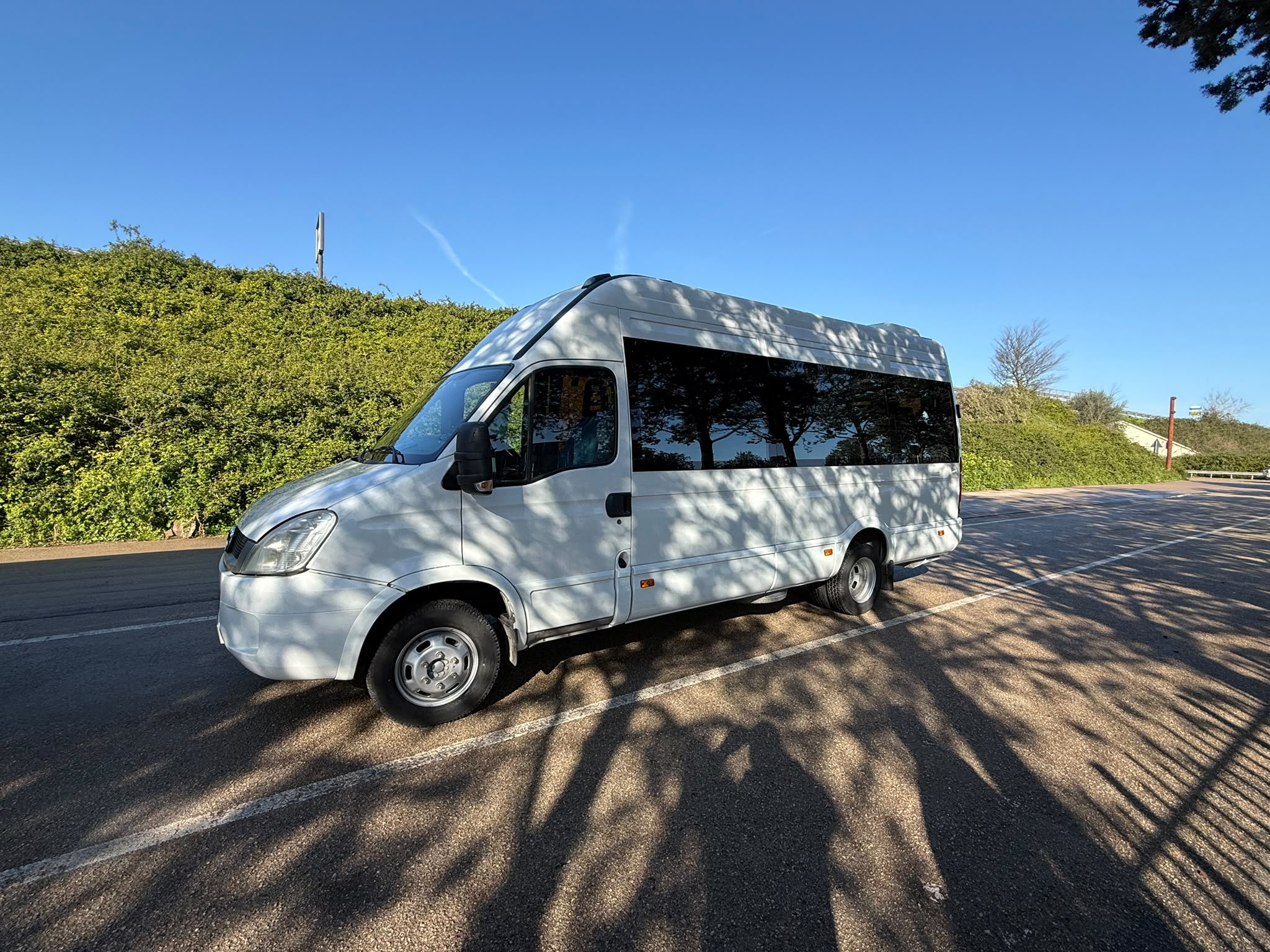 A white bus parked in a parking lot with a green landscape in the background