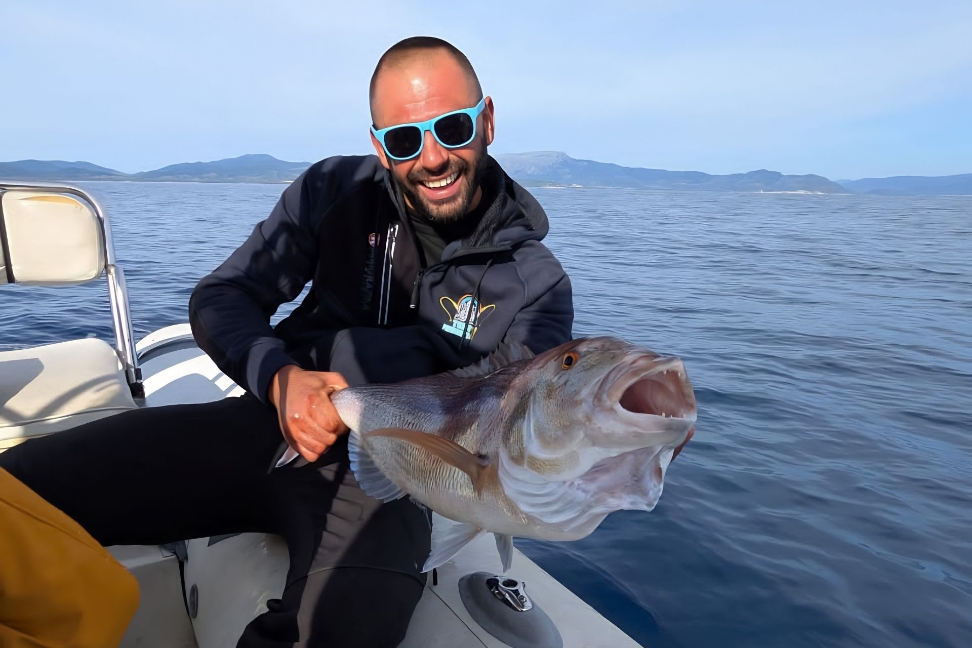 Man with a fish just caught in Sardinia, sitting on a boat with his guide.