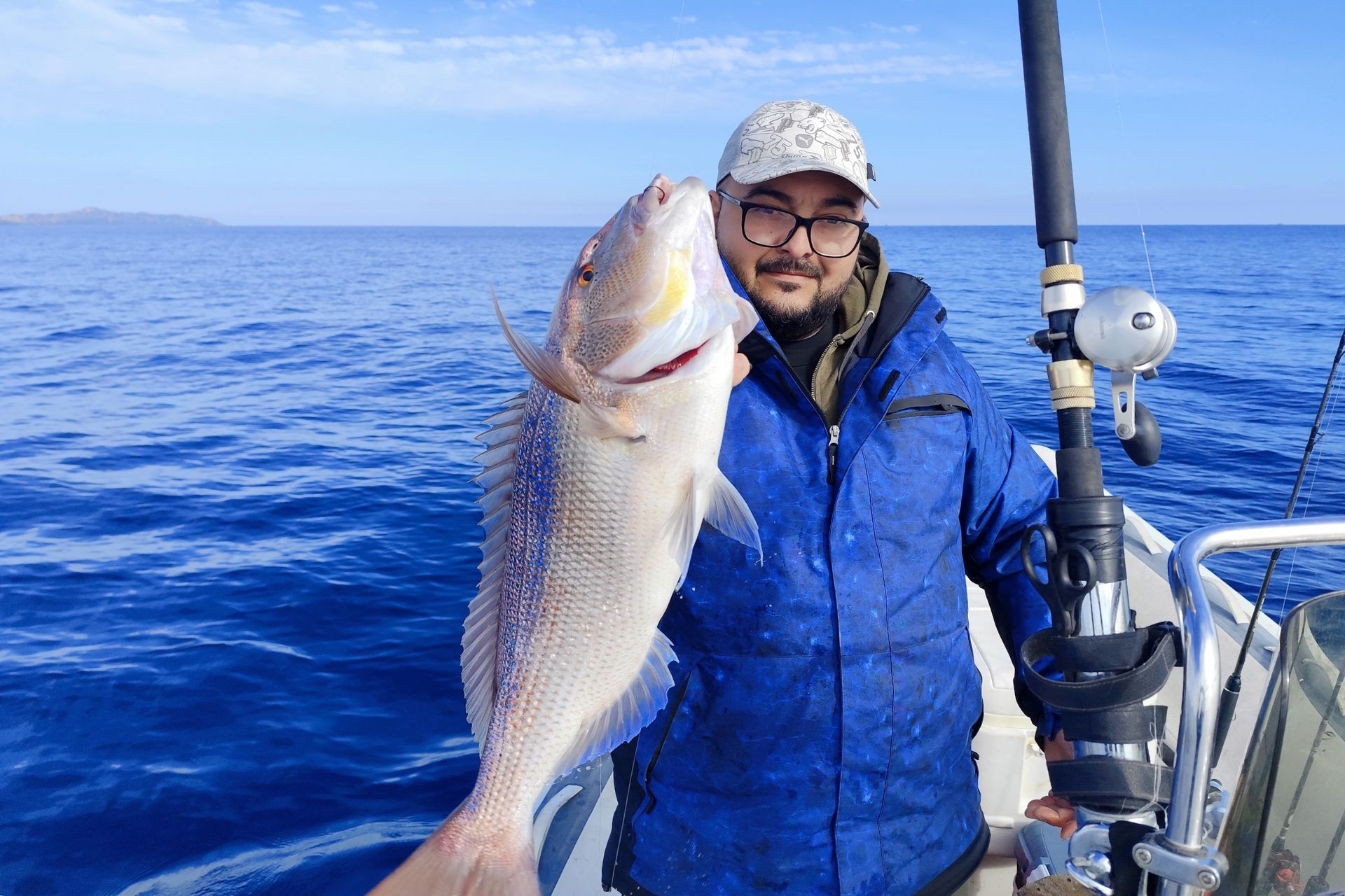 Man with a fish just caught in Sardinia, in blue water and blue sky with a few clouds.
