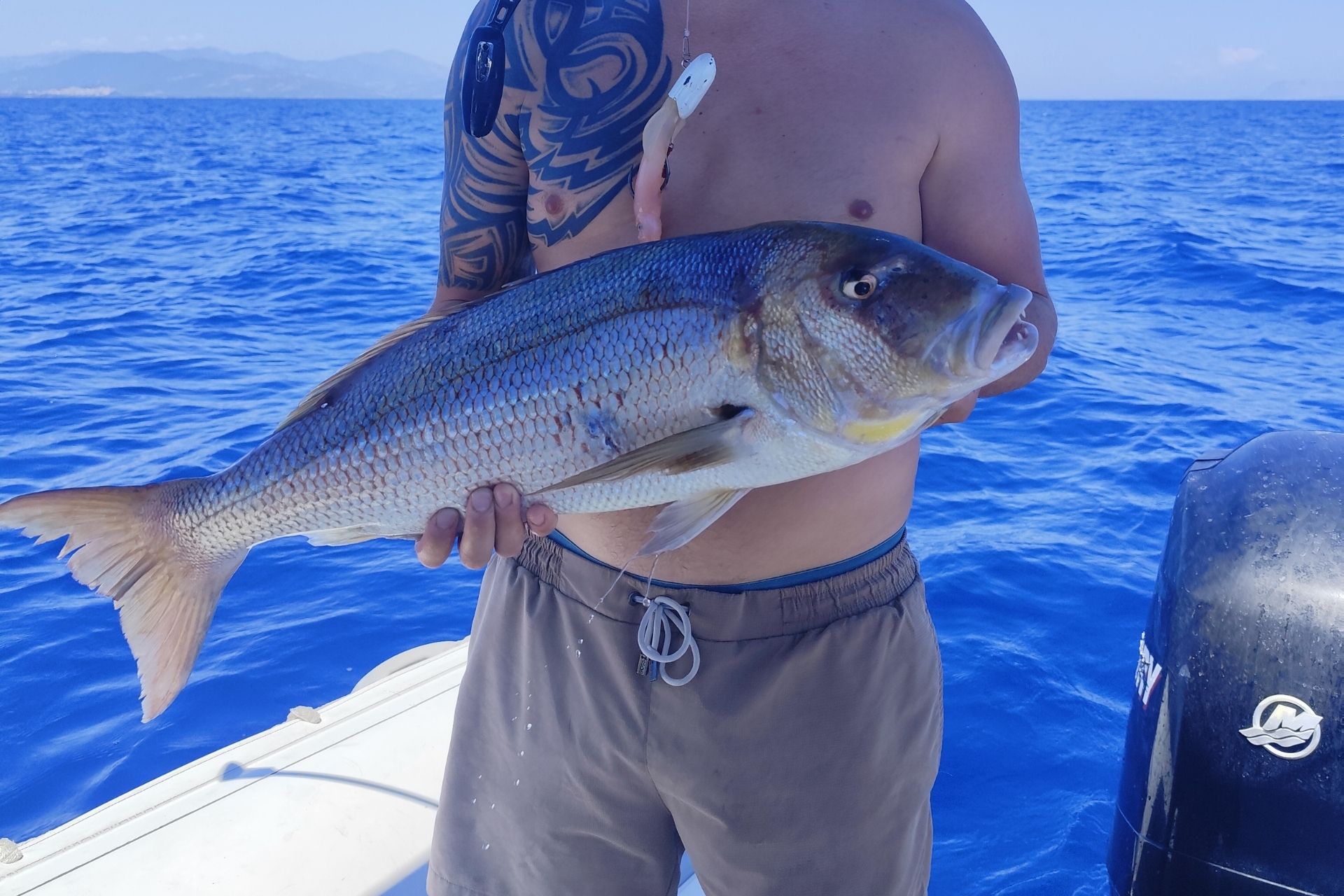 A shirtless man with a freshly caught fish in his hand on a motor boat