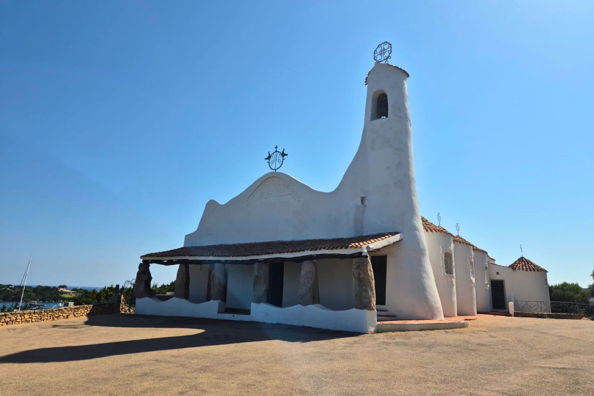 A white church with a bell tower and a thatched roof, surrounded by a stone fence and located in a landscape with granite boulders