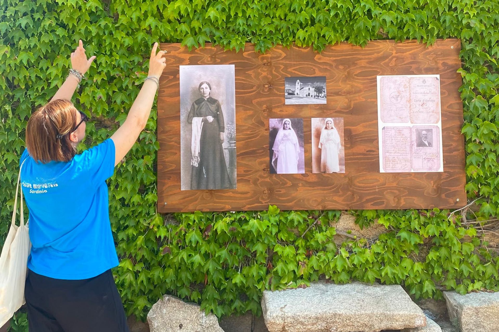 A woman with a shoulder bag touches an information panel with images of women in traditional clothing and historical documents