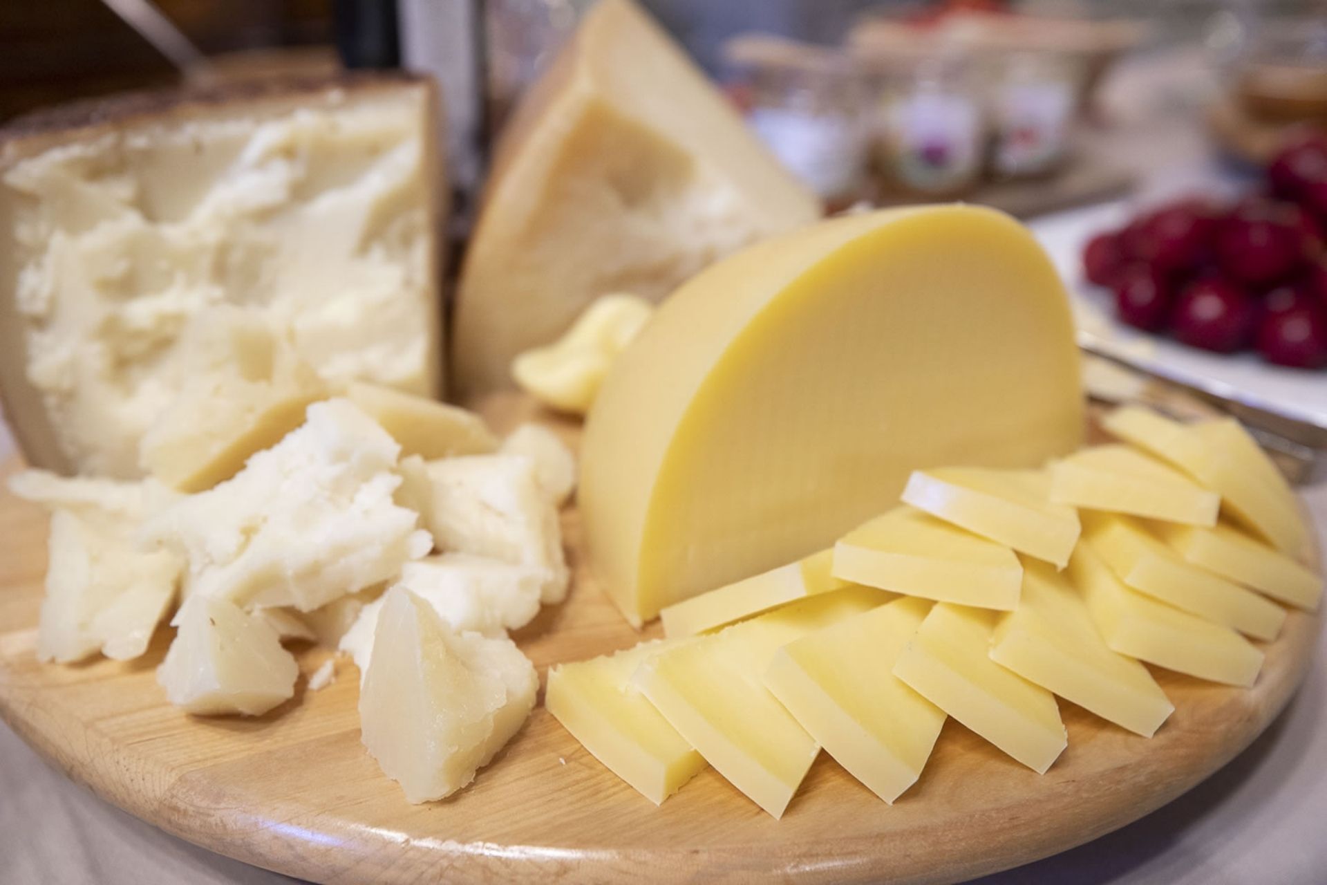Diversas formas de queso dispuestas sobre una tabla de cortar de madera, con otros quesos y frutas