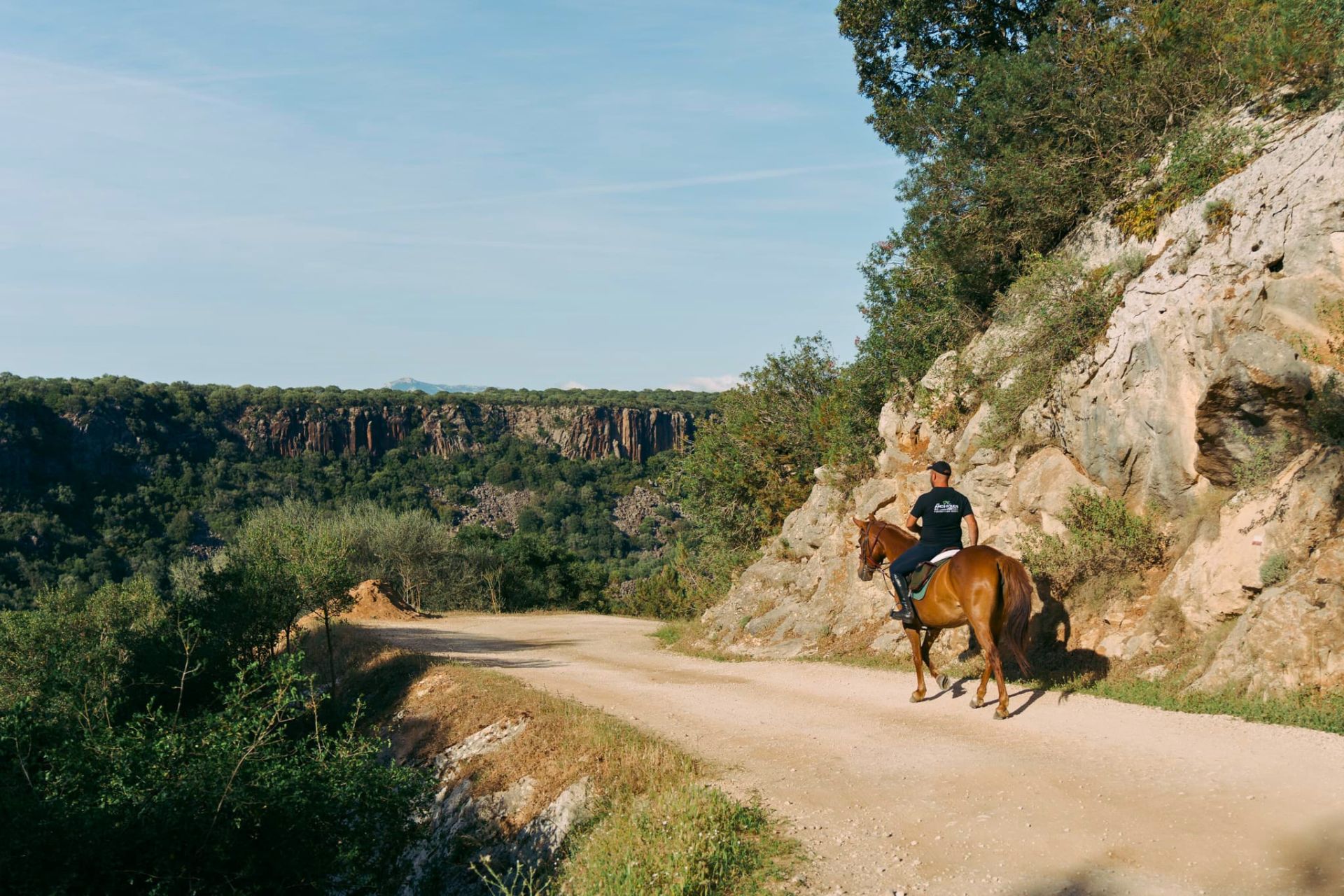 Uomo a cavallo su una strada sterrata in un paesaggio naturale con alberi e rocce