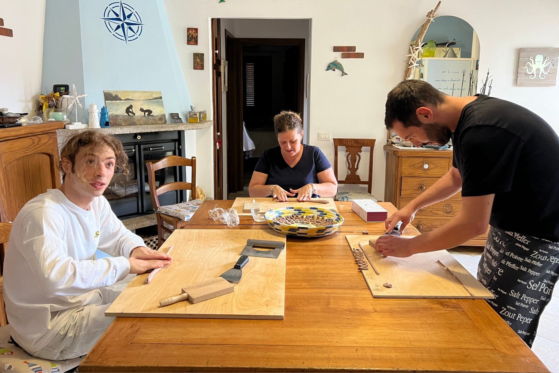 Three people sitting at a table in the kitchen, with tools and ingredients for fresh pasta.