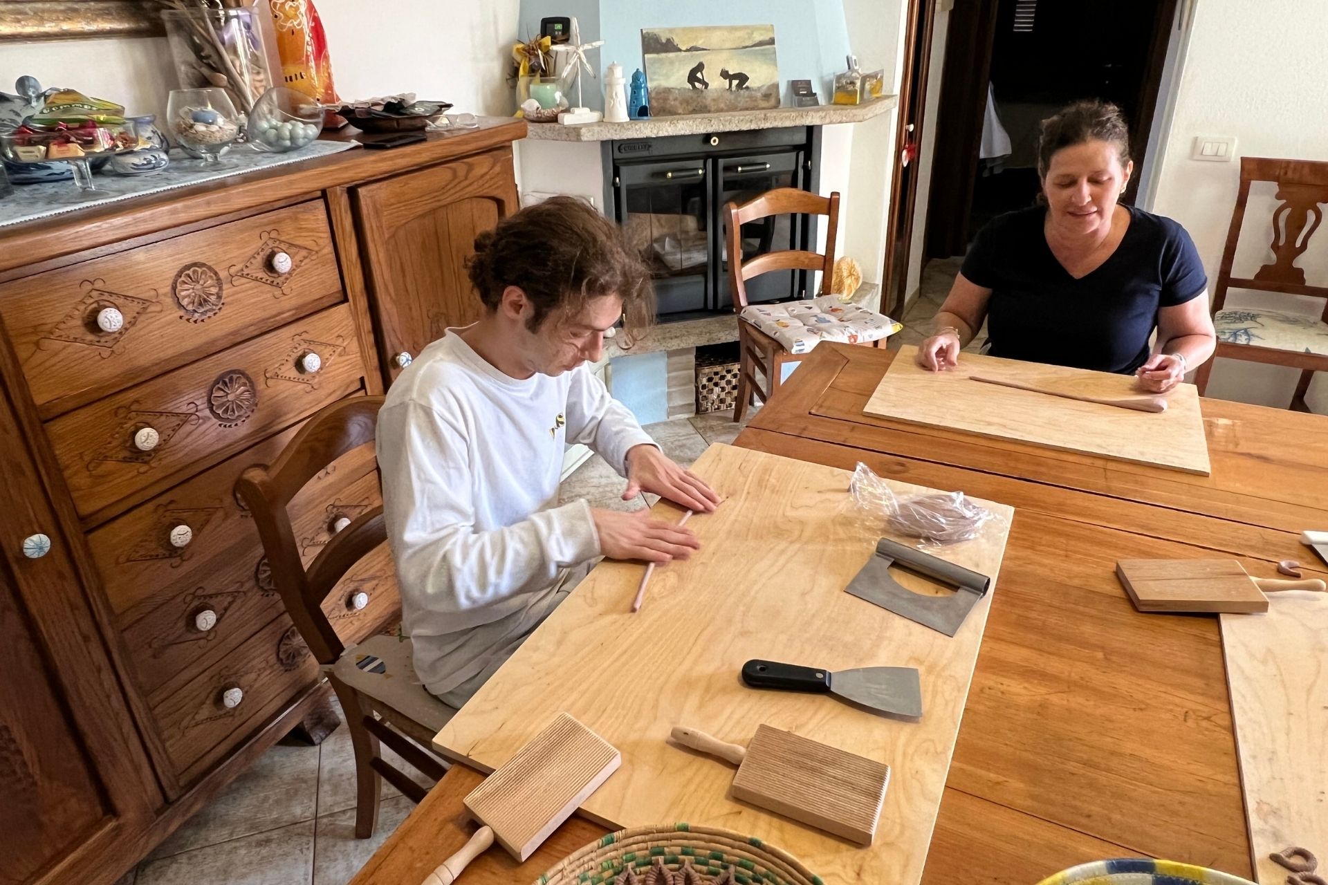 Two people work at a table with kitchen utensils and pasta ingredients.