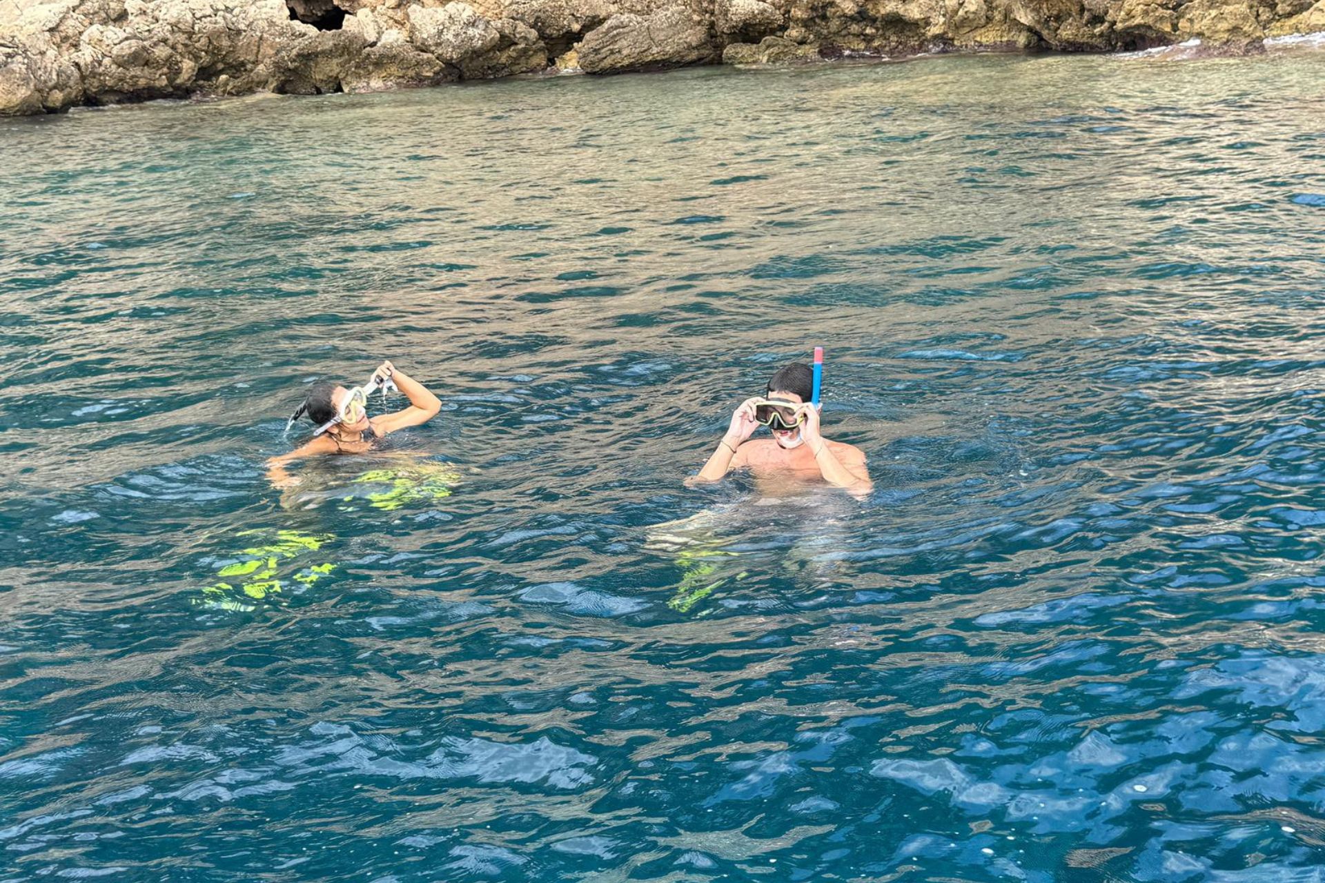 Due persone in acqua con maschera e boccaglio, circondate da rocce e mare cristallino