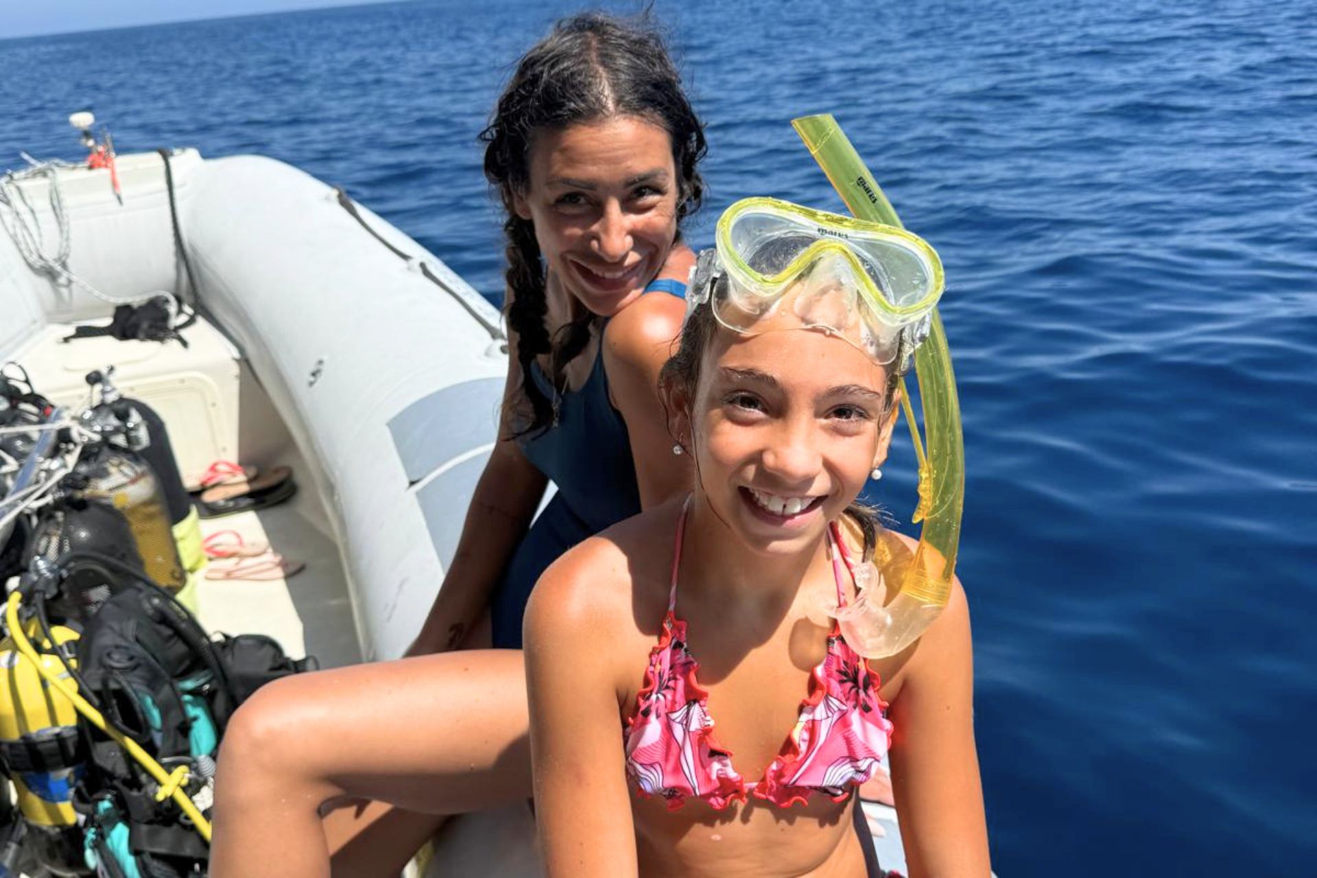 Due ragazze sorridenti su un gommone con attrezzatura da snorkeling, sullo sfondo un mare azzurro e limpido