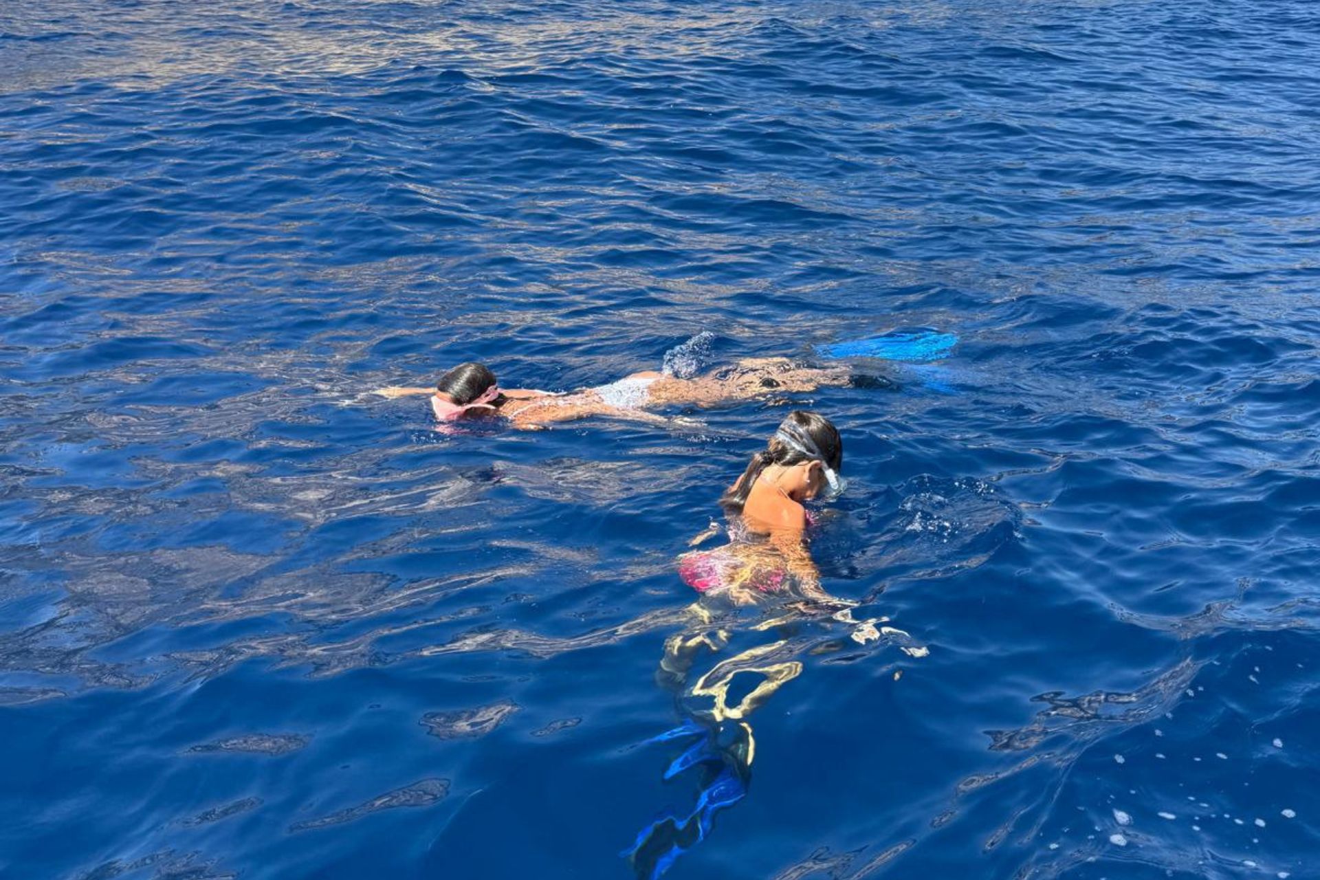 Due donne in costume da bagno stanno facendo snorkeling in mare aperto, con maschera e boccaglio, circondate da acque limpide e blu