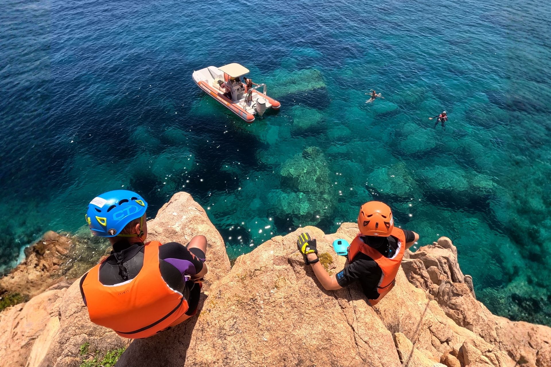Due persone in giacca di salvataggio e casco si godono la vista del mare azzurro e delle rocce granitiche di Cala di Volpe sulla Costa Smeralda.