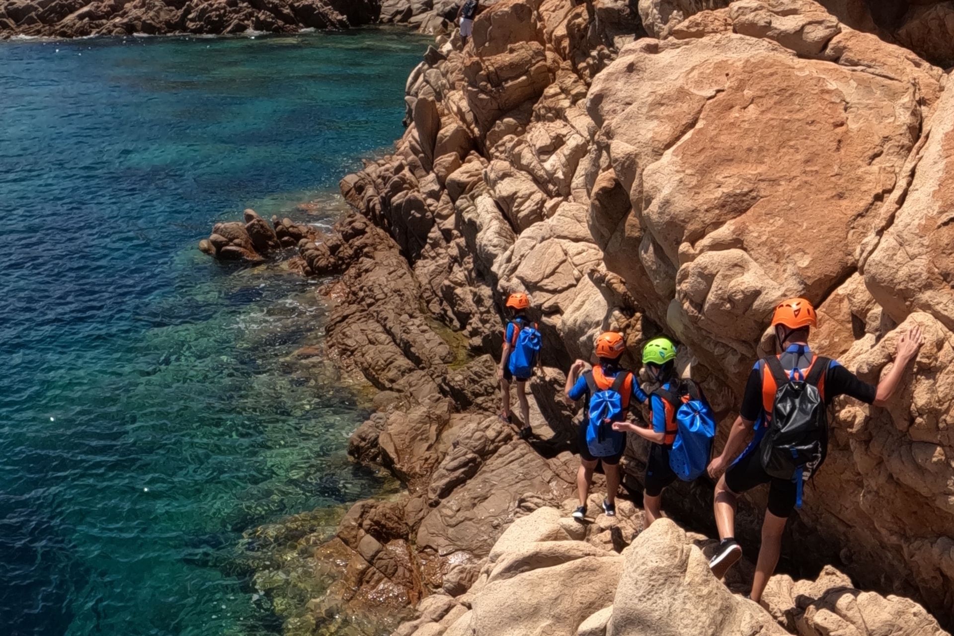 Un gruppo di persone con caschi e zaini si arrampica su una scogliera vicino al mare.