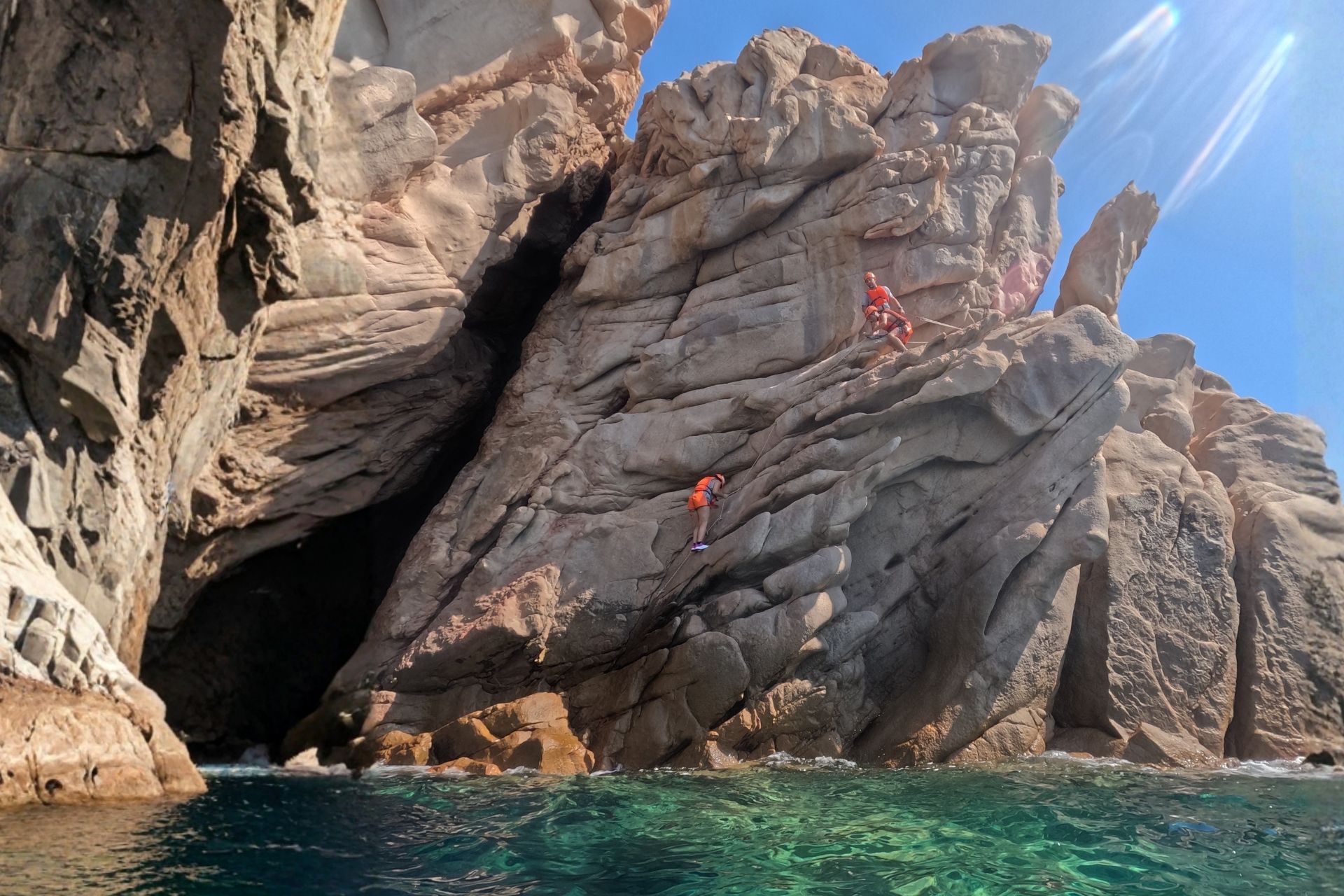 Due persone in abbigliamento da coasteering si avventurano su una scogliera rocciosa a picco sul mare.