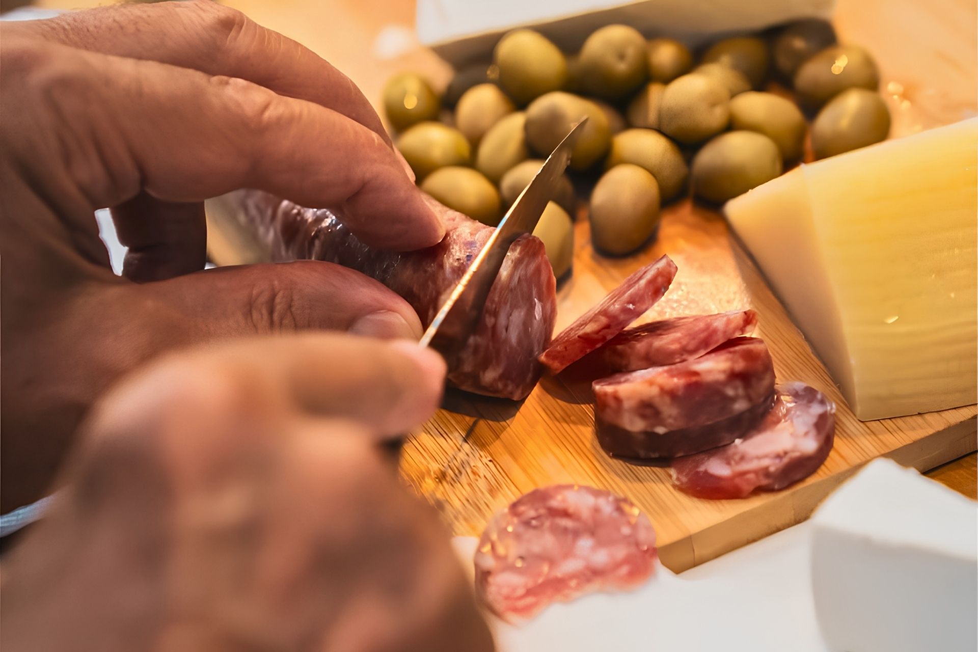 Une personne coupe du salami sur une planche à découper avec d'autres aliments.