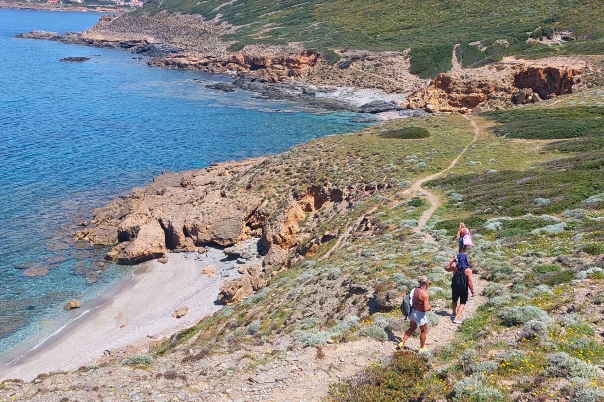 Drei Personen wandern auf einem Küstenweg mit Blick auf das Meer und die Klippen auf Sardinien