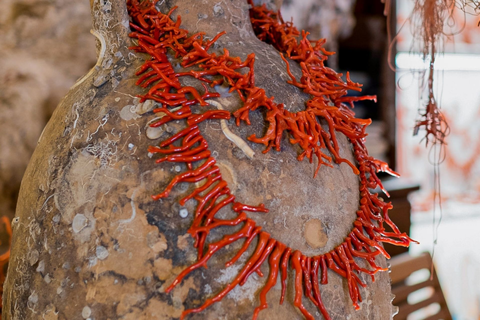Una scultura decorata con corallo rosso su sfondo marrone. Sullo sfondo una stanza con mobili.
