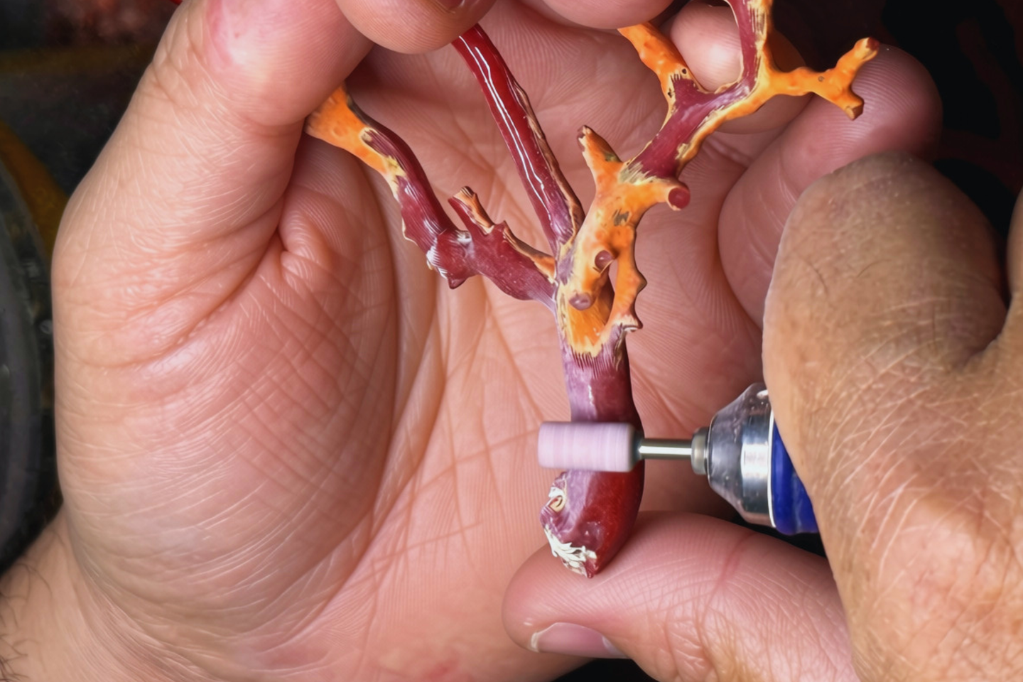 Persona che lavora un pezzo di corallo rosso con una lima elettrica
