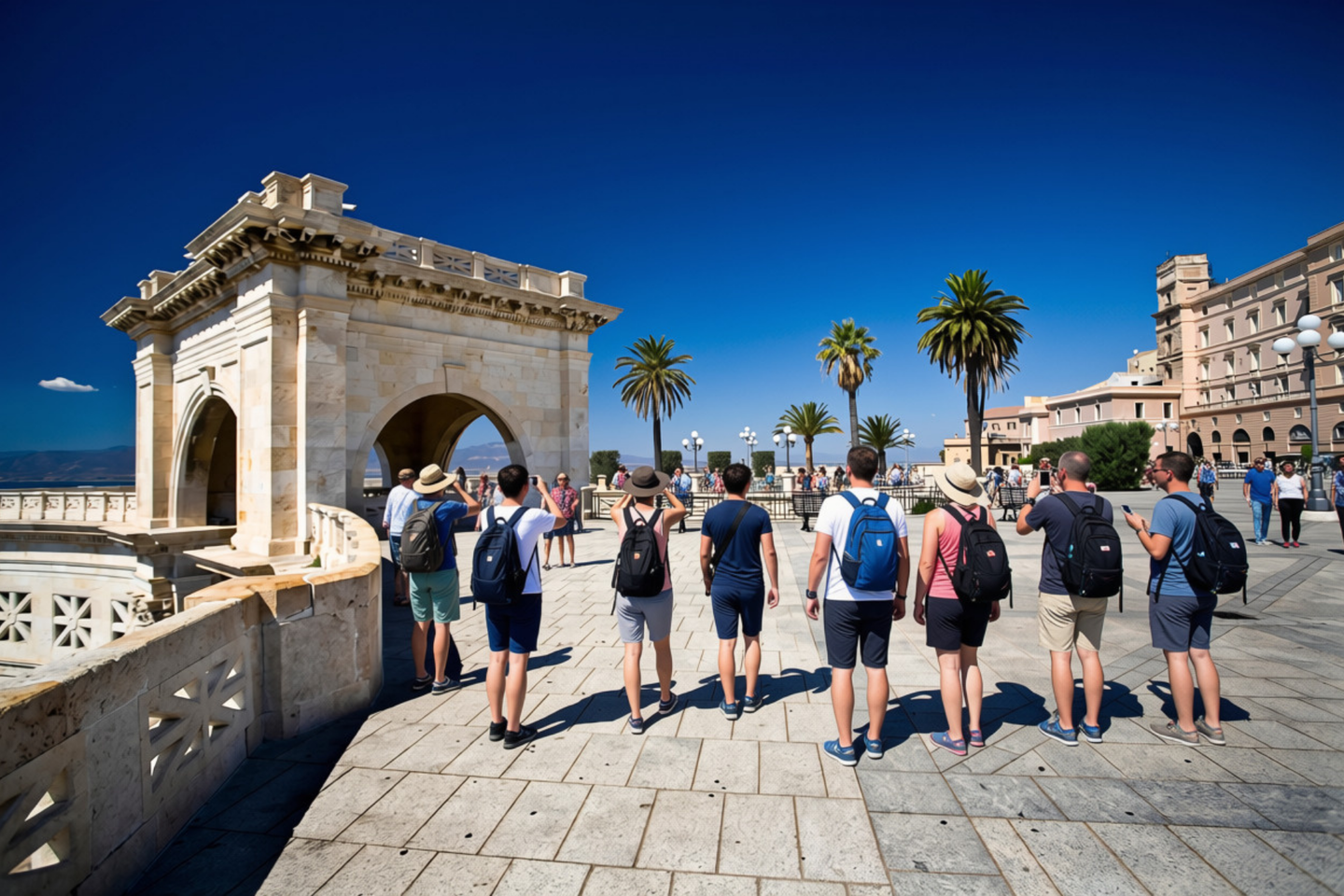 Un grupo de personas camina por una terraza panorámica con un arco de piedra y palmeras de fondo.