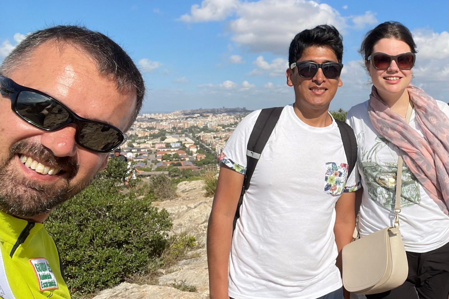 Tres personas sonrientes en la cima de una colina con vistas a la ciudad de Cagliari, Cerdeña, Italia.