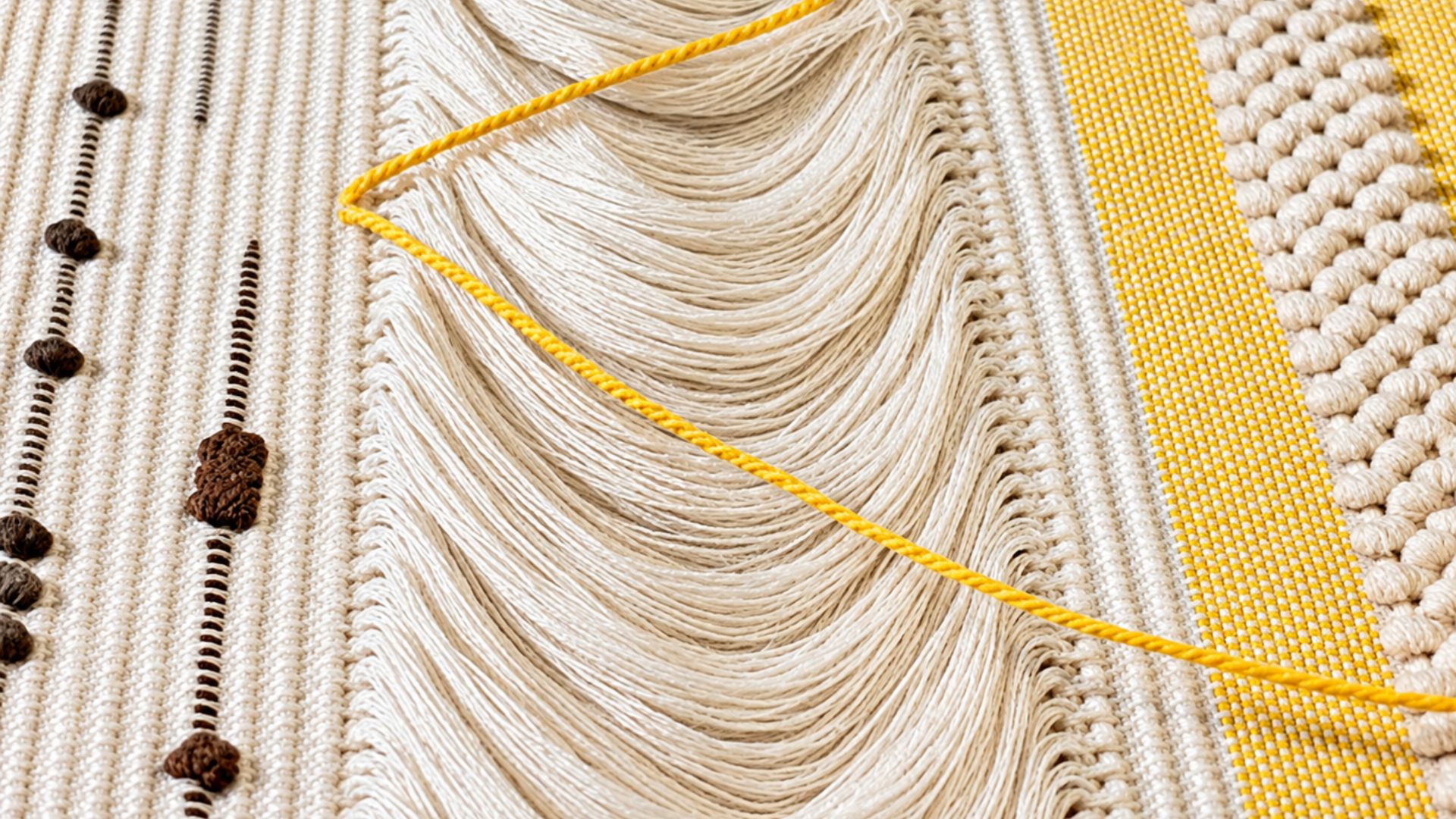 Immagine di un arazzo con frange e motivi geometrici in bianco, giallo e marrone