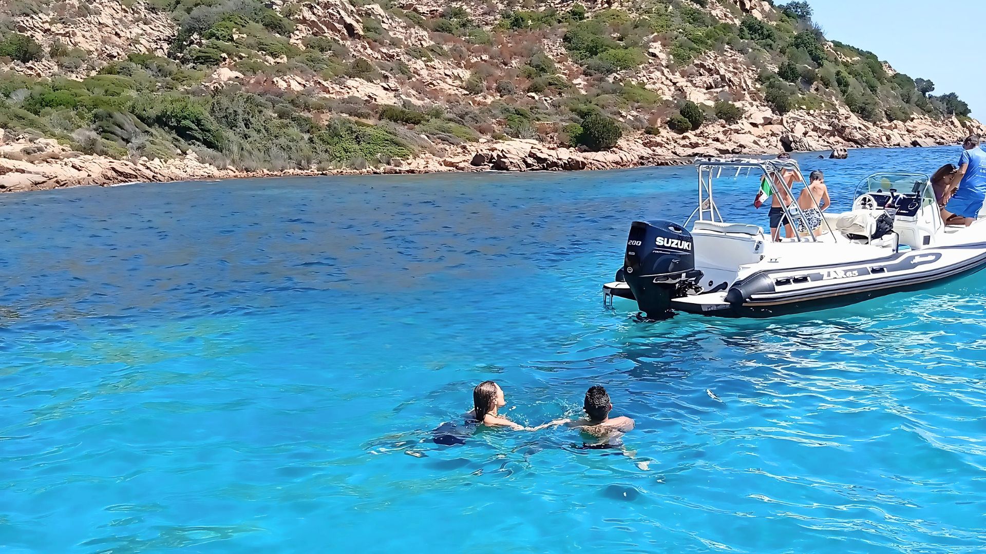 Zwei Personen schwimmen im türkisfarbenen Wasser mit einem Beiboot im Hintergrund
