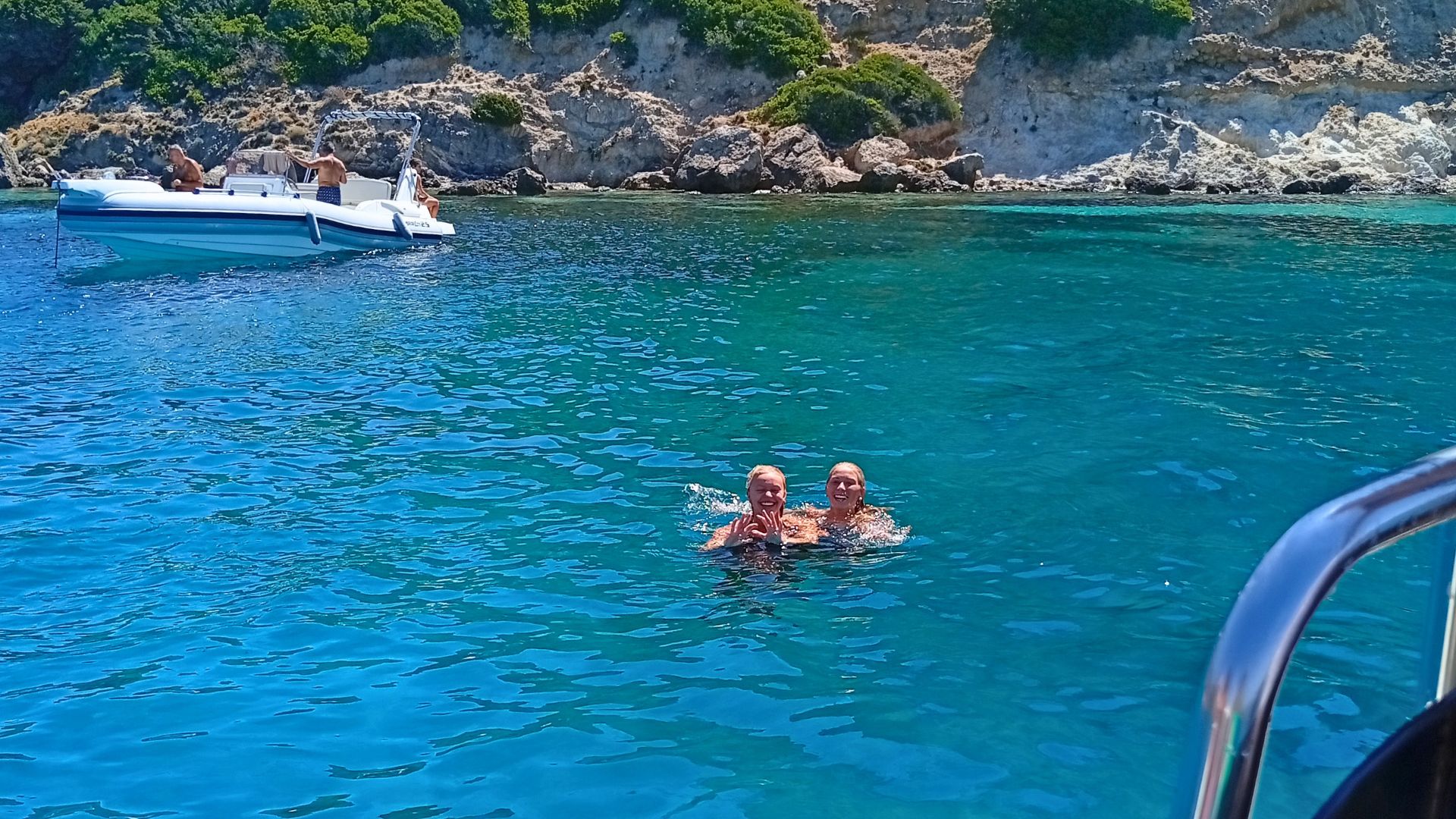 Zwei Personen schwimmen im türkisfarbenen Meer mit einem Beiboot im Hintergrund